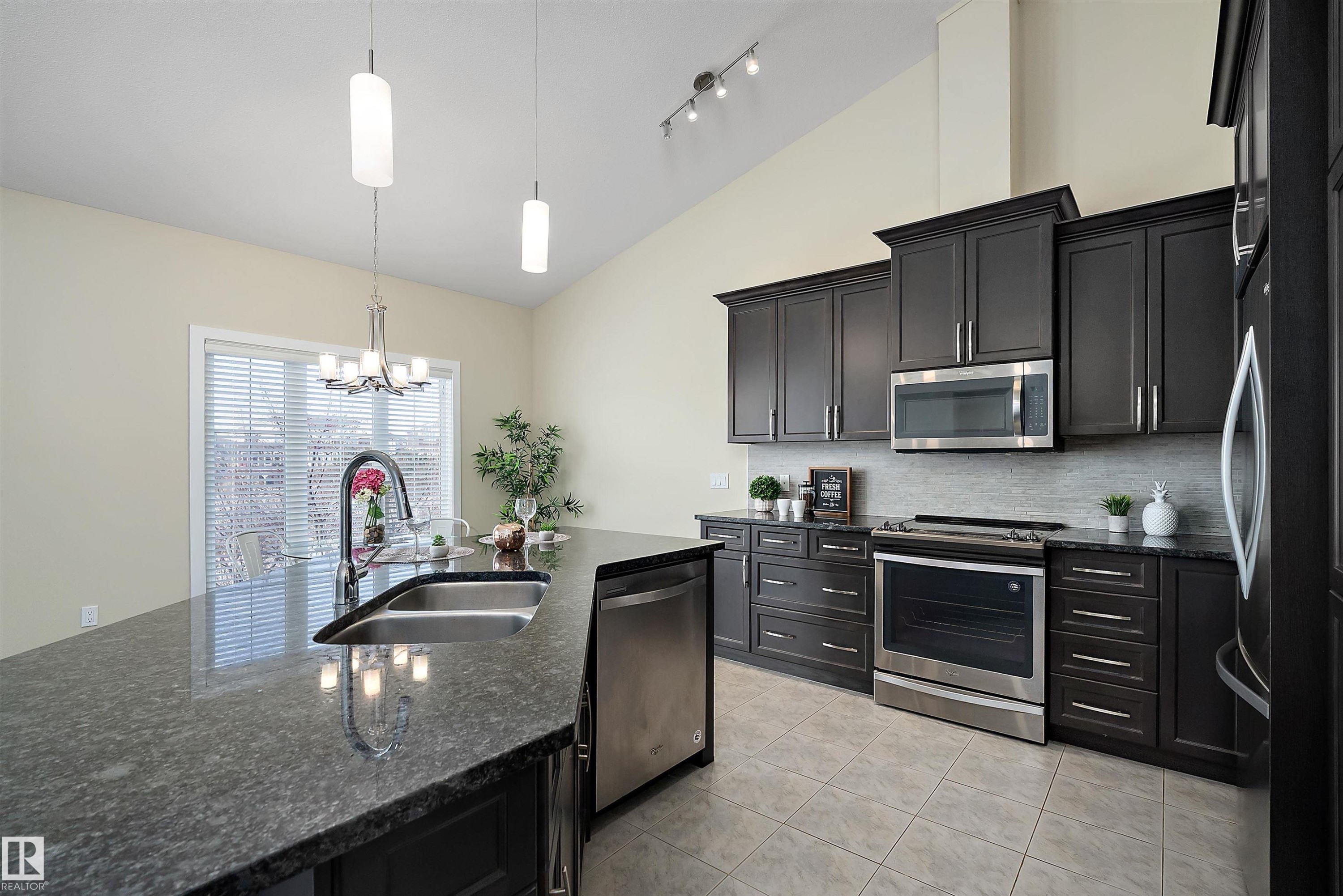 Kitchen featuring dark cabinetry, stainless steel appliances, and a central island with an undermount sink - 14 3090 Cameron Heights Way, Edmonton, AB - Indoor Photo Showing Kitchen With Double Sink With Upgraded Kitchen