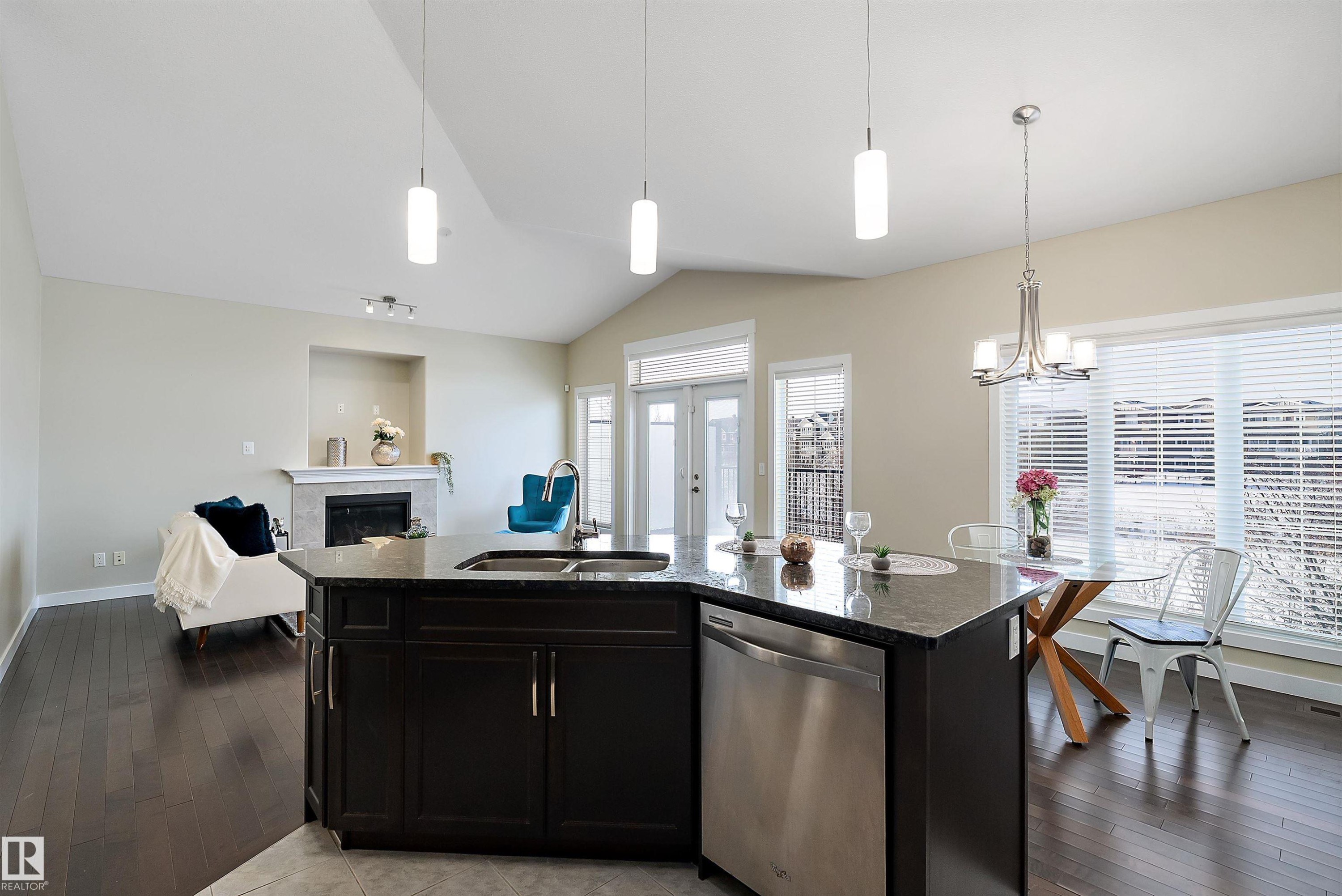 Kitchen island with a dark stone-finish countertop, undermount stainless steel sink, and integrated dishwasher - 14 3090 Cameron Heights Way, Edmonton, AB - Indoor Photo Showing Kitchen With Double Sink