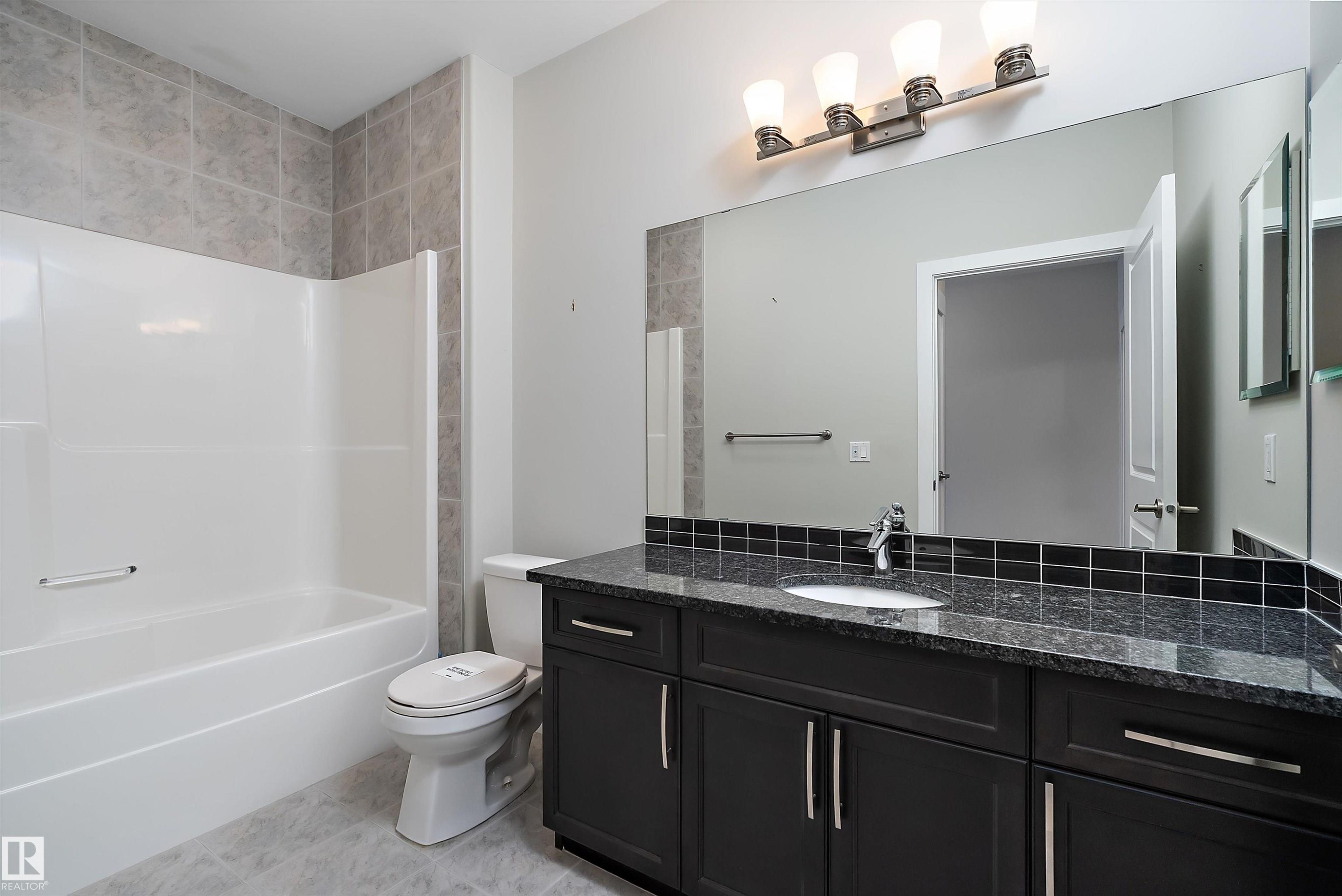 Bathroom featuring a built-in bathtub with a white surround, a toilet, and a vanity with dark cabinetry - 14 3090 Cameron Heights Way, Edmonton, AB - Indoor Photo Showing Bathroom