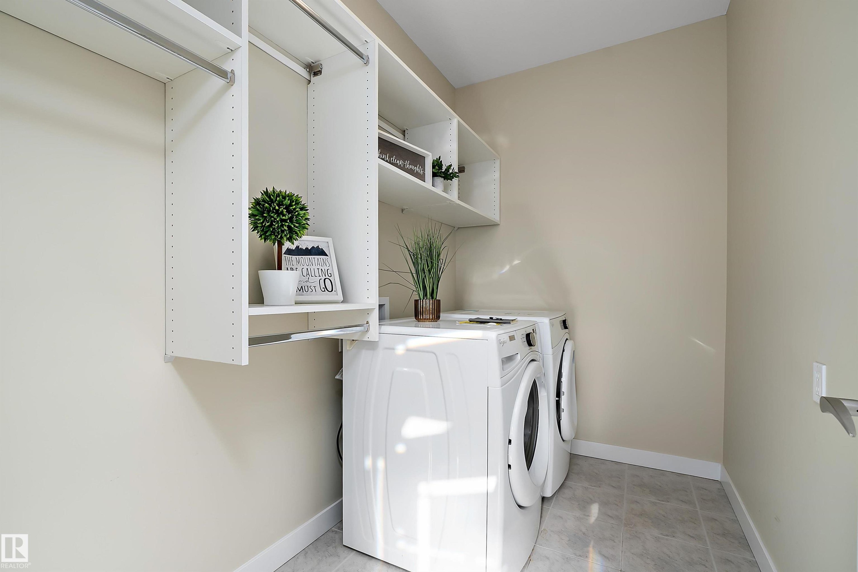 Dedicated laundry area featuring white front-load appliances, integrated shelving, hanging rods, and light-toned tile flooring - 14 3090 Cameron Heights Way, Edmonton, AB - Indoor Photo Showing Laundry Room