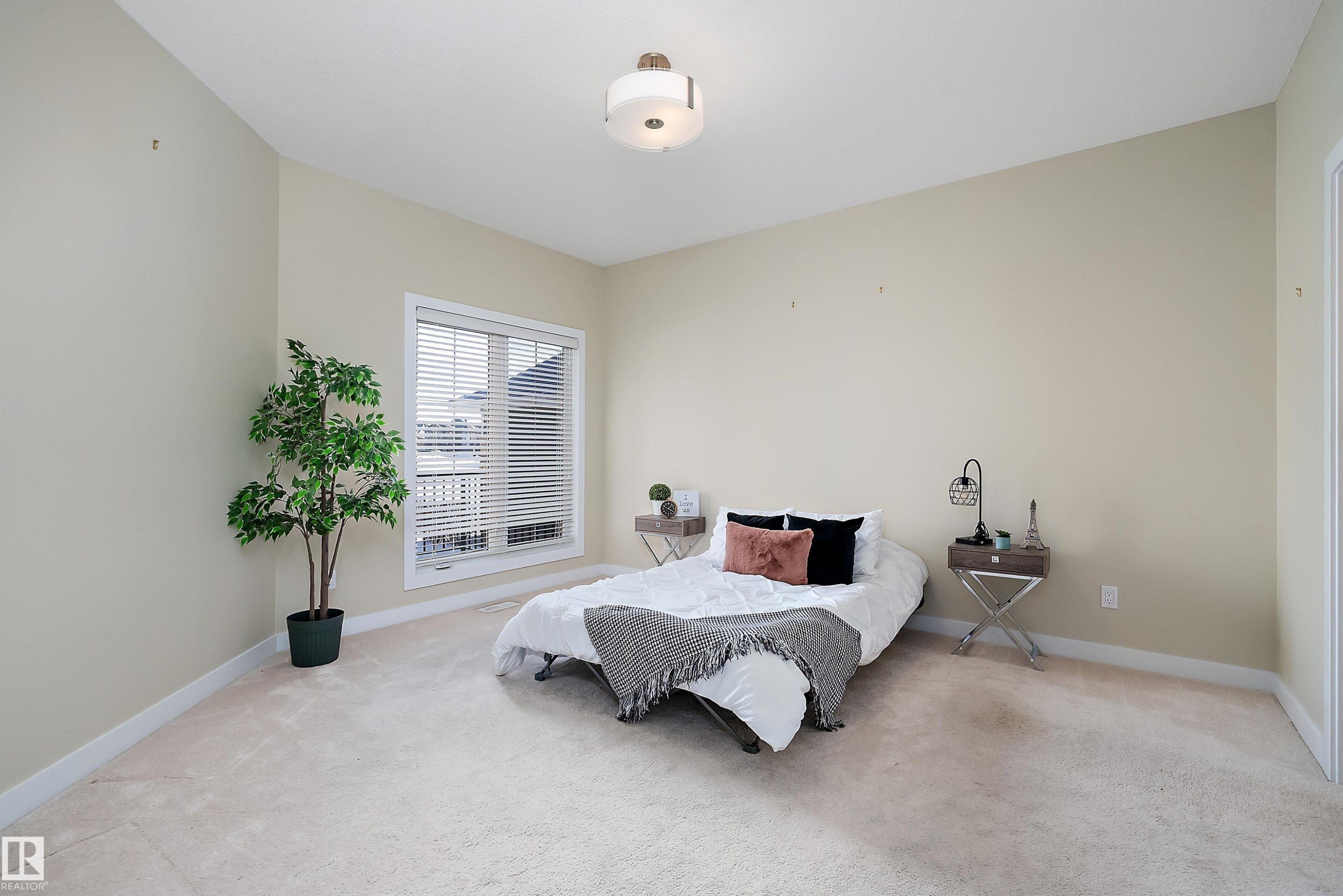 Carpeted room with a double-pane window featuring white blinds, a contemporary ceiling light fixture, and neutral wall paint - 14 3090 Cameron Heights Way, Edmonton, AB - Indoor Photo Showing Bedroom