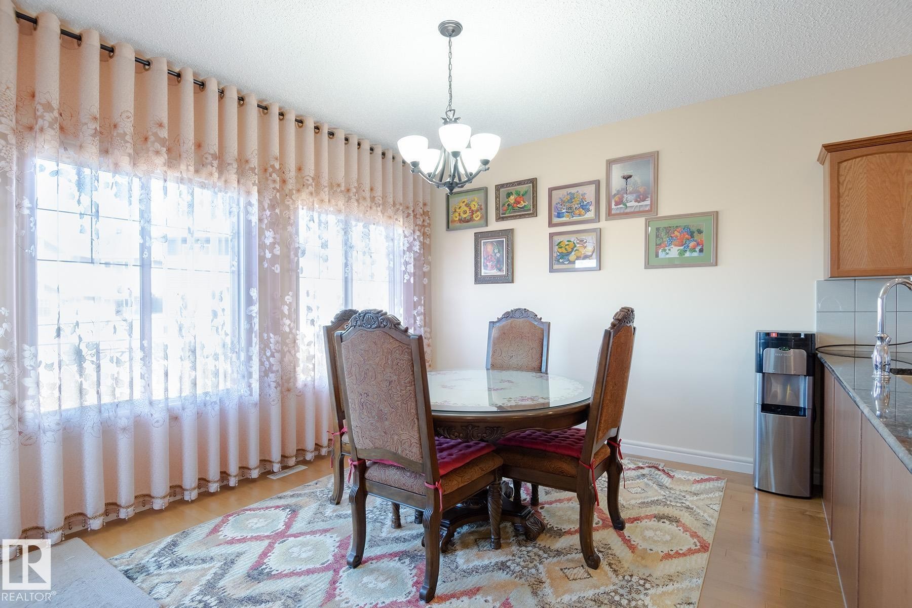 Dining area featuring wood-finish flooring, a wall of large windows with privacy drapes, and a chandelier light fixture - 7426 Getty Way, Edmonton, AB - Indoor Photo Showing Dining Room