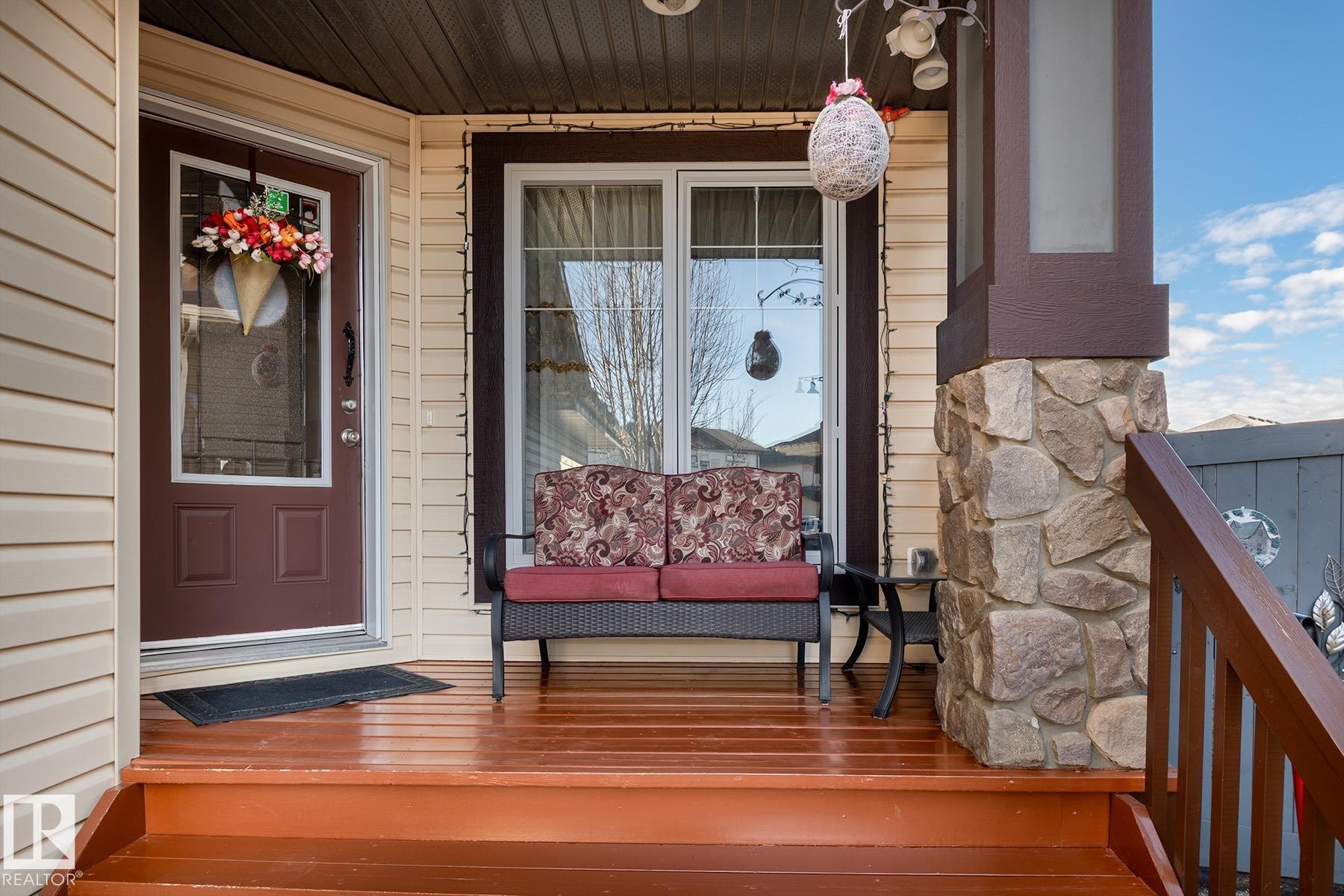 Welcoming front porch featuring a rich wood-finish deck and steps, a stone-clad pillar, and beige vinyl siding - 7426 Getty Way, Edmonton, AB - Outdoor With Deck Patio Veranda With Exterior