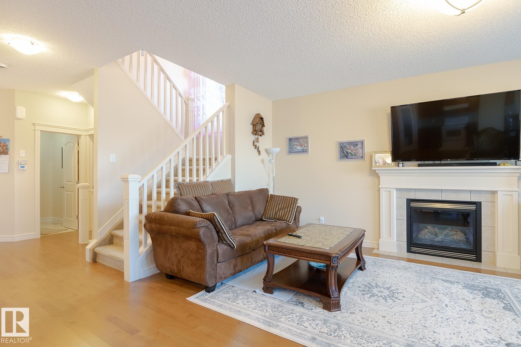 Living area featuring a fireplace with a mantel, wood-finish flooring, and a staircase with white railings - 7426 Getty Way, Edmonton, AB - Indoor Photo Showing Living Room With Fireplace