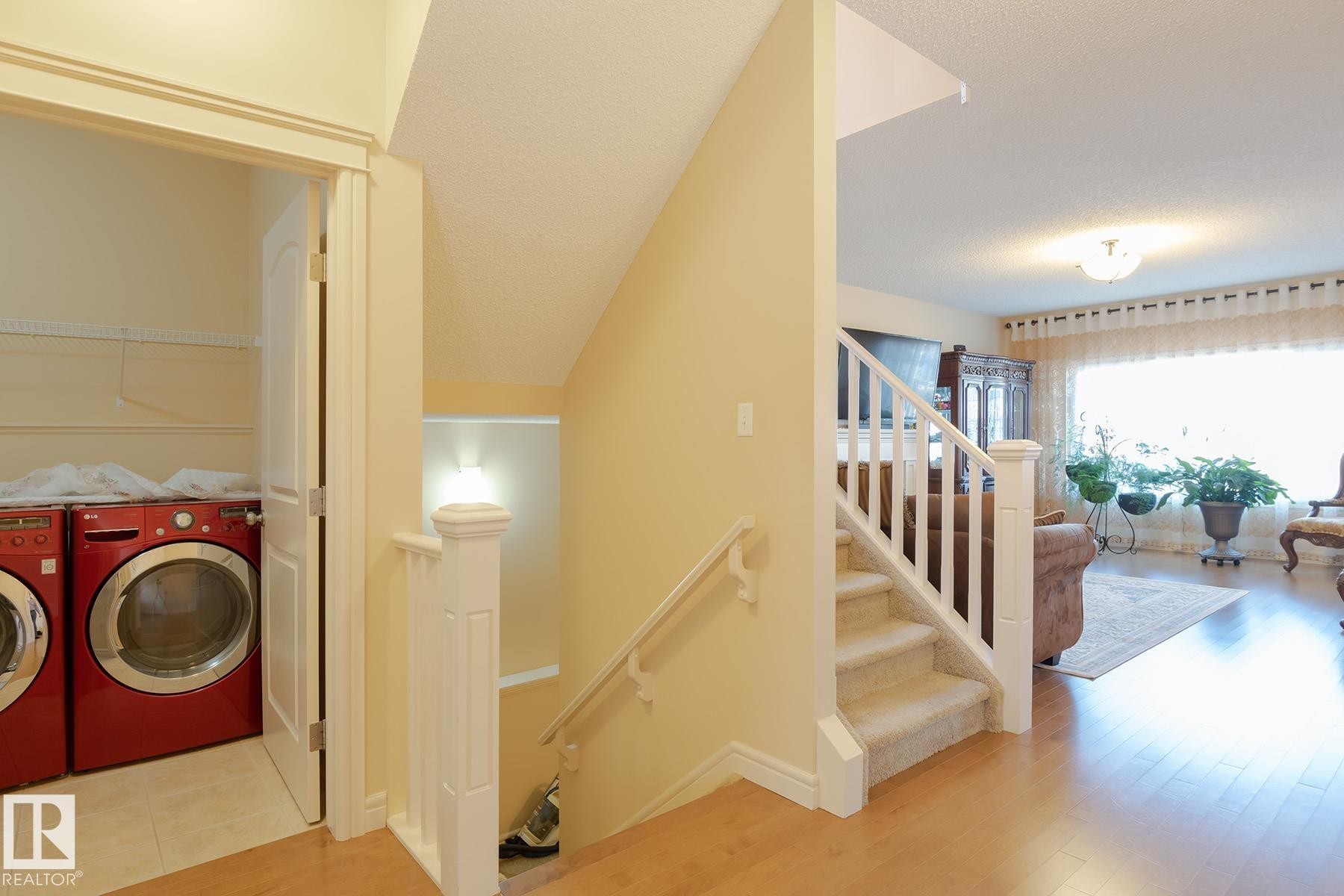 Carpeted staircase with white balusters and handrail, light wood-finish flooring, and an adjacent laundry area featuring a tile floor - 7426 Getty Way, Edmonton, AB - Indoor Photo Showing Other Room