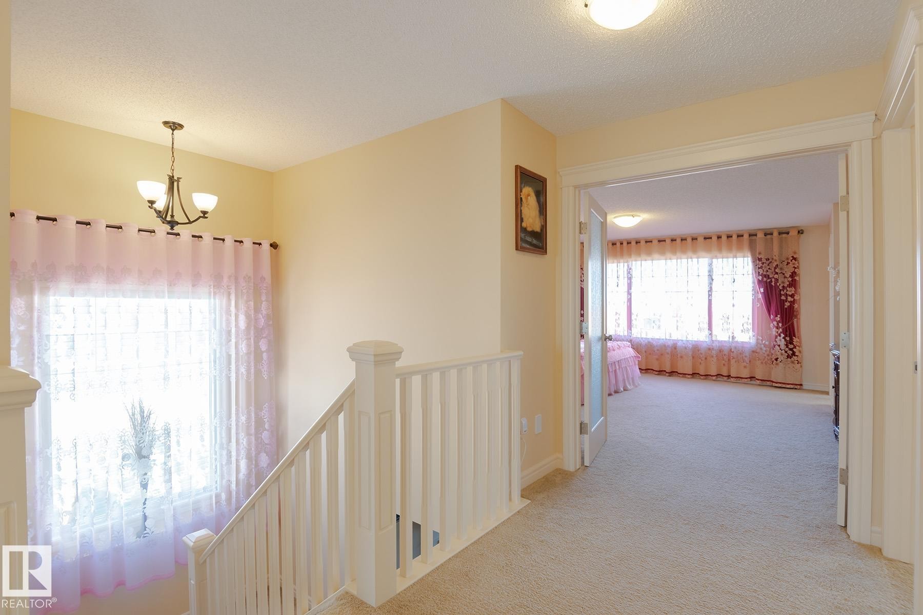 Carpeted hallway with white banister leading to an open doorway with frosted glass French doors - 7426 Getty Way, Edmonton, AB - Indoor Photo Showing Other Room