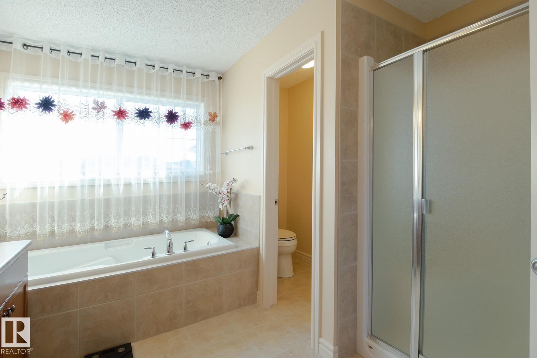 Bathroom featuring a built-in soaking tub with deck-mounted fixtures, a separate shower with a frosted glass enclosure, and tiled flooring - 7426 Getty Way, Edmonton, AB - Indoor Photo Showing Bathroom