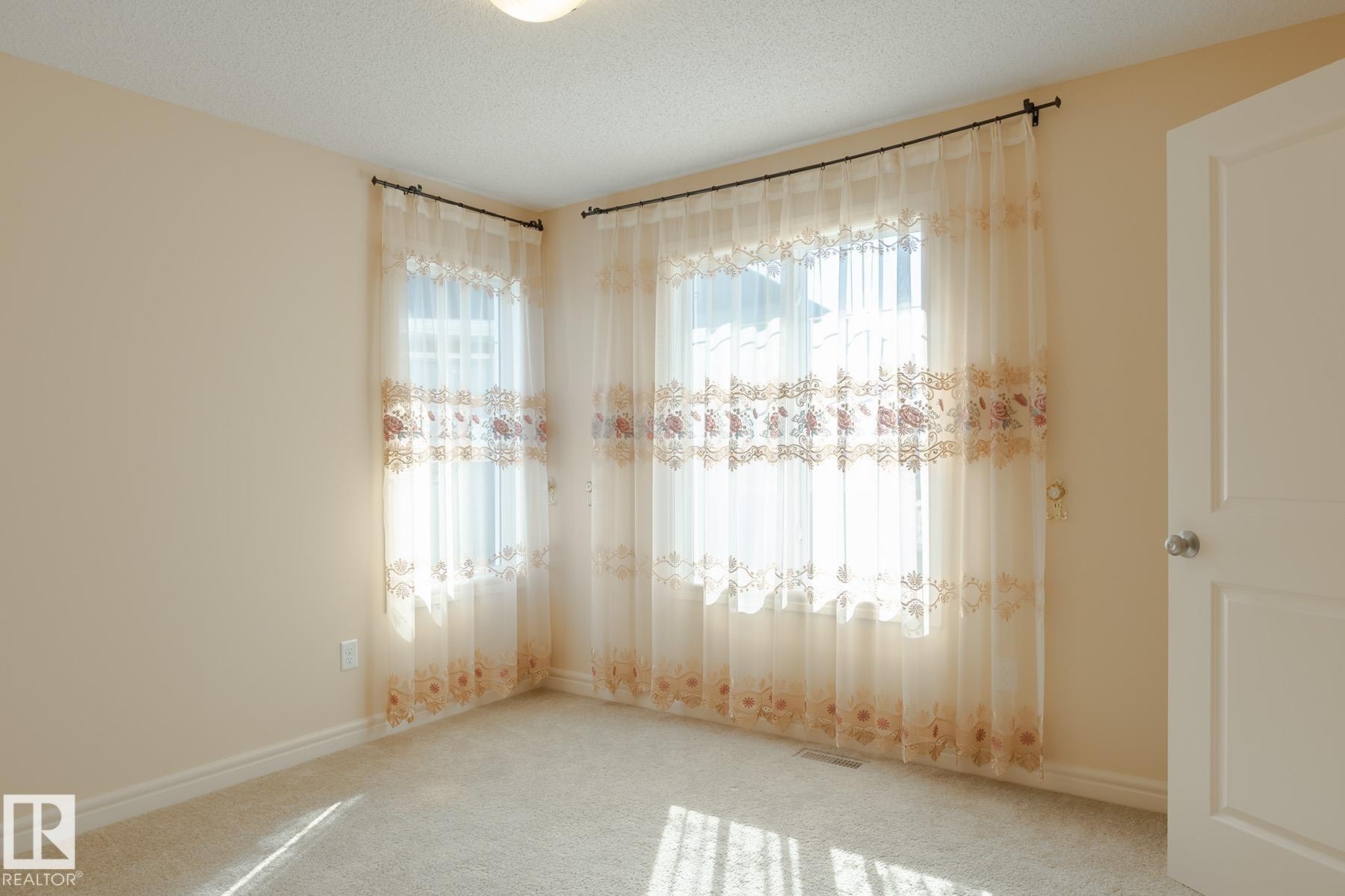 Room featuring two windows with sheer curtains, neutral-toned walls, and light-colored carpet flooring - 7426 Getty Way, Edmonton, AB - Indoor Photo Showing Other Room