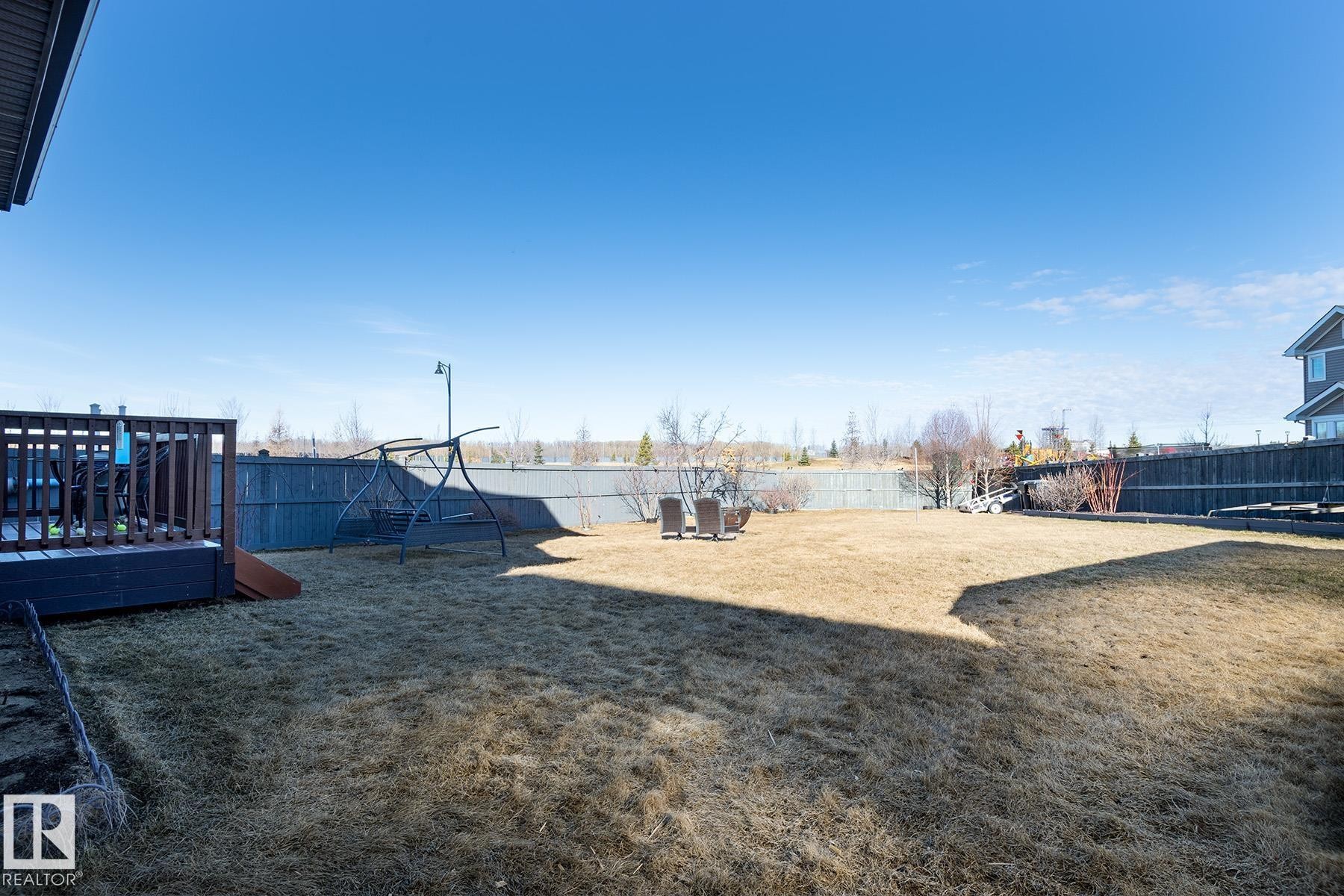 Spacious backyard featuring a large elevated wood deck, expansive lawn area, full perimeter fencing, and mature shrubbery - 7426 Getty Way, Edmonton, AB - Outdoor