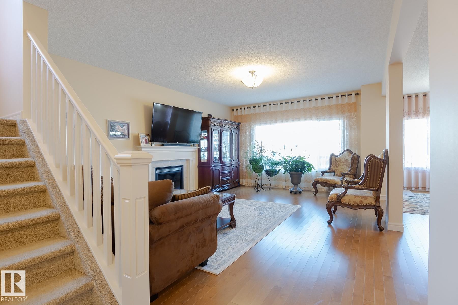Bright living area featuring wood-finish flooring, a white mantel fireplace, and a large window - 7426 Getty Way, Edmonton, AB - Indoor Photo Showing Living Room With Fireplace