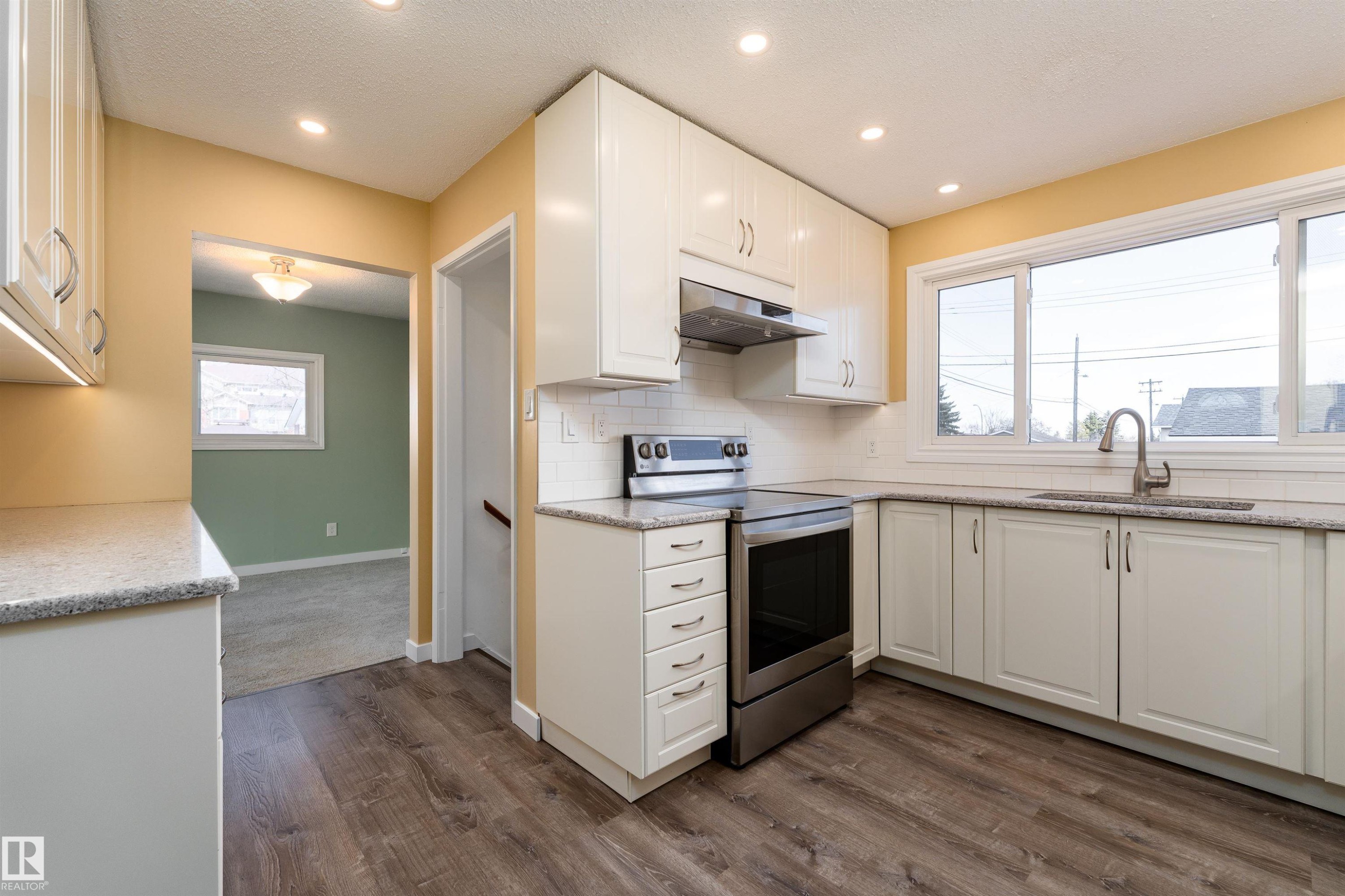 Modern kitchen featuring wood-finish flooring, white cabinetry with contemporary hardware, stainless steel appliances, and a white subway tile backsplash - 13331 64 Street Nw, Edmonton, AB - Indoor Photo Showing Kitchen