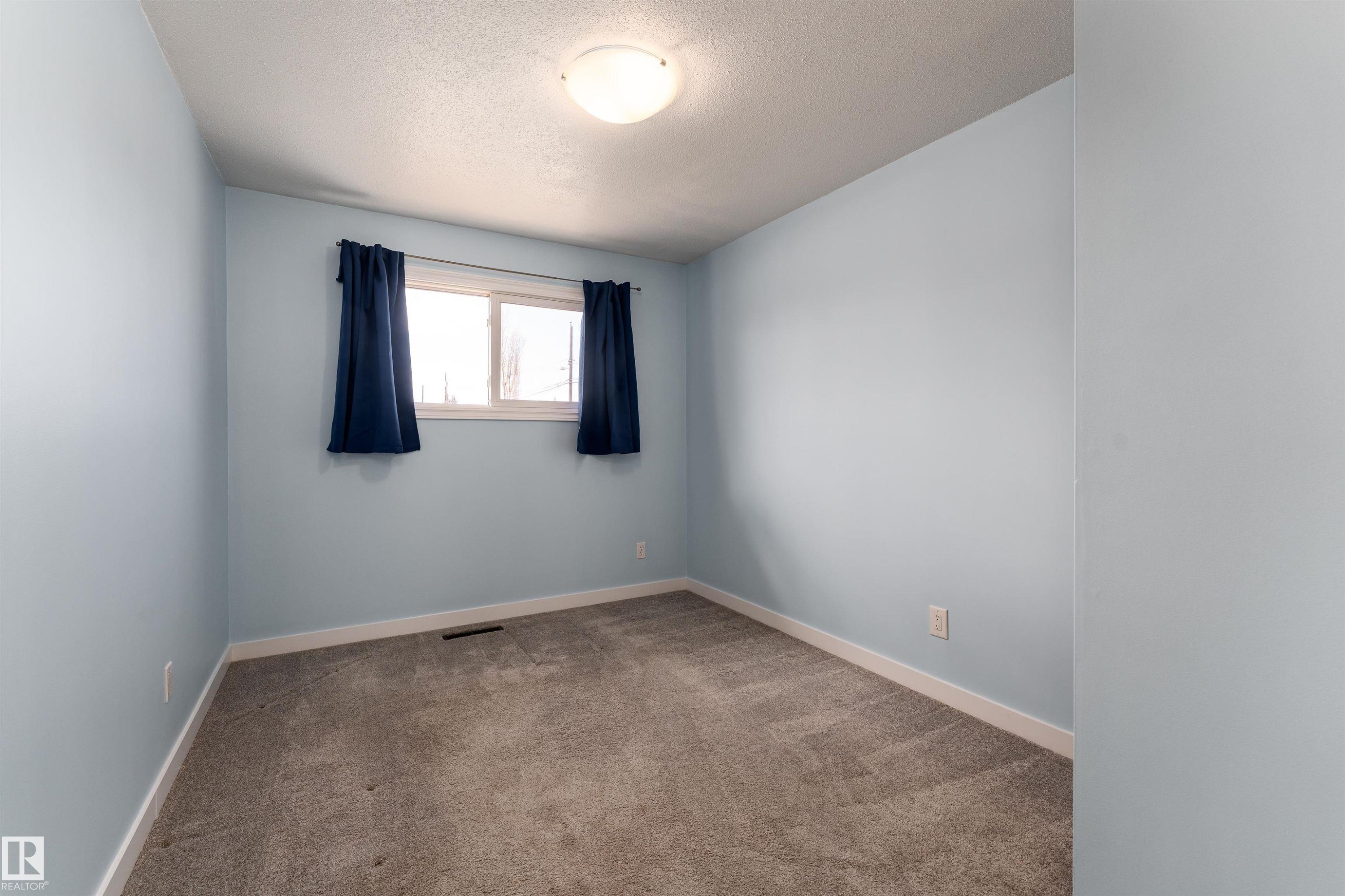 Carpeted room featuring light blue walls, white trim, and a double window with dark blue curtains - 13331 64 Street Nw, Edmonton, AB - Indoor Photo Showing Other Room