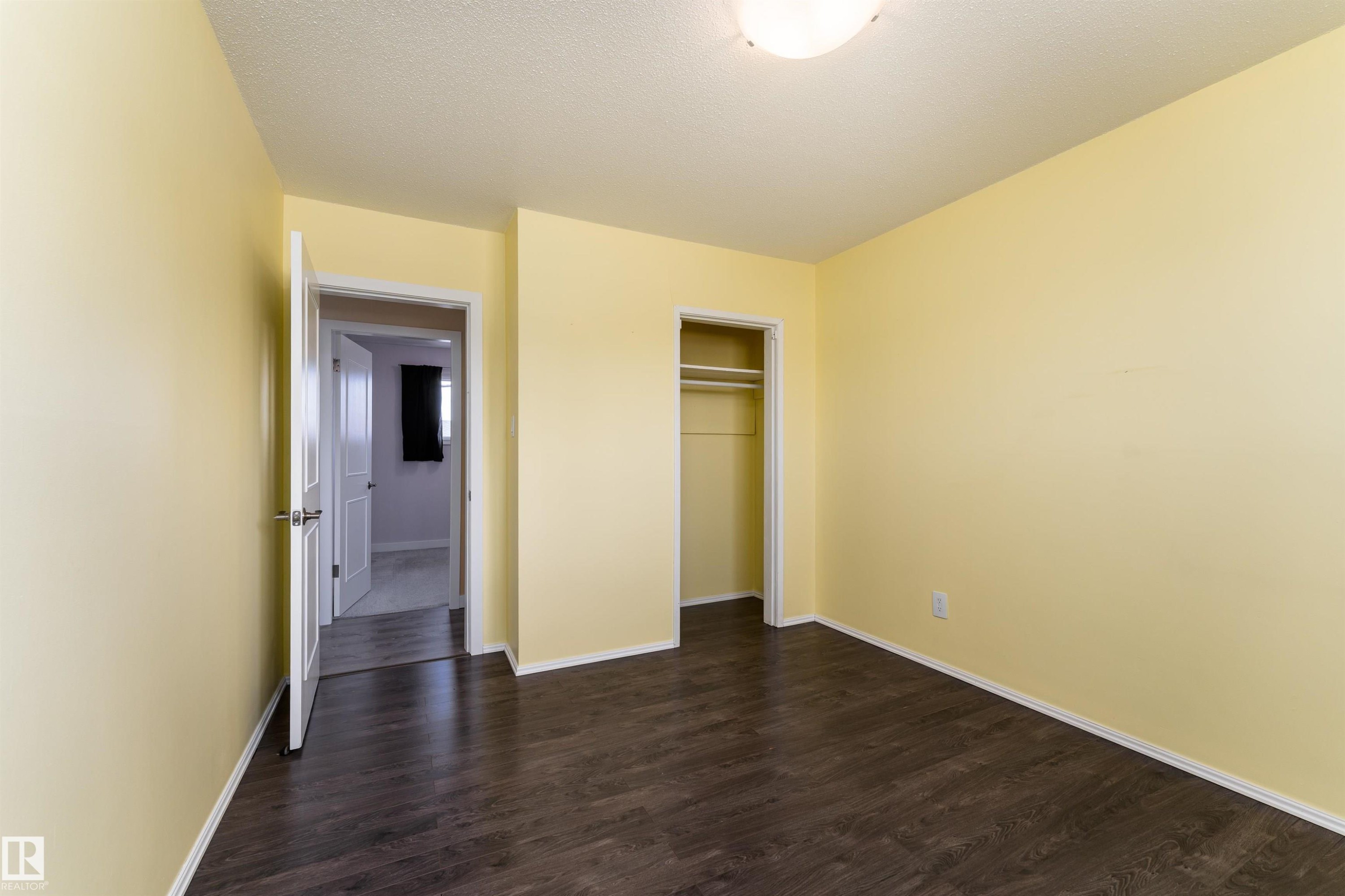 Spacious room featuring wood-finish flooring, light yellow walls, white baseboards, and a built-in closet with shelving and hanging rod - 13331 64 Street Nw, Edmonton, AB - Indoor Photo Showing Other Room