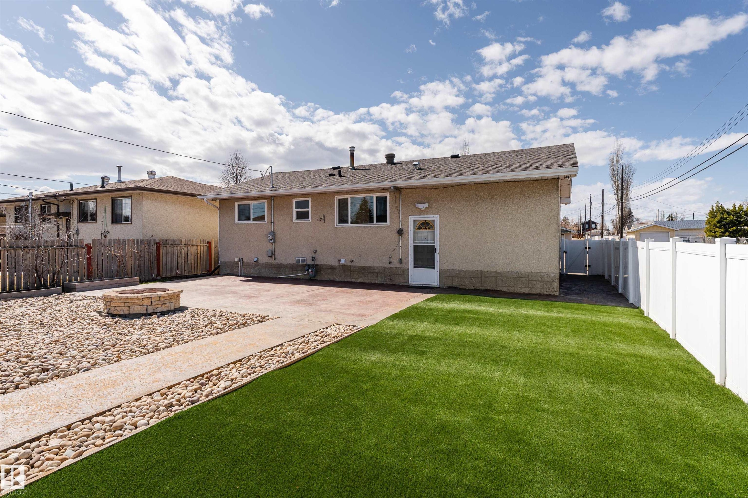 Expansive rear yard featuring an artificial turf lawn, a concrete patio, and a stone fire pit area - 13331 64 Street Nw, Edmonton, AB - Outdoor