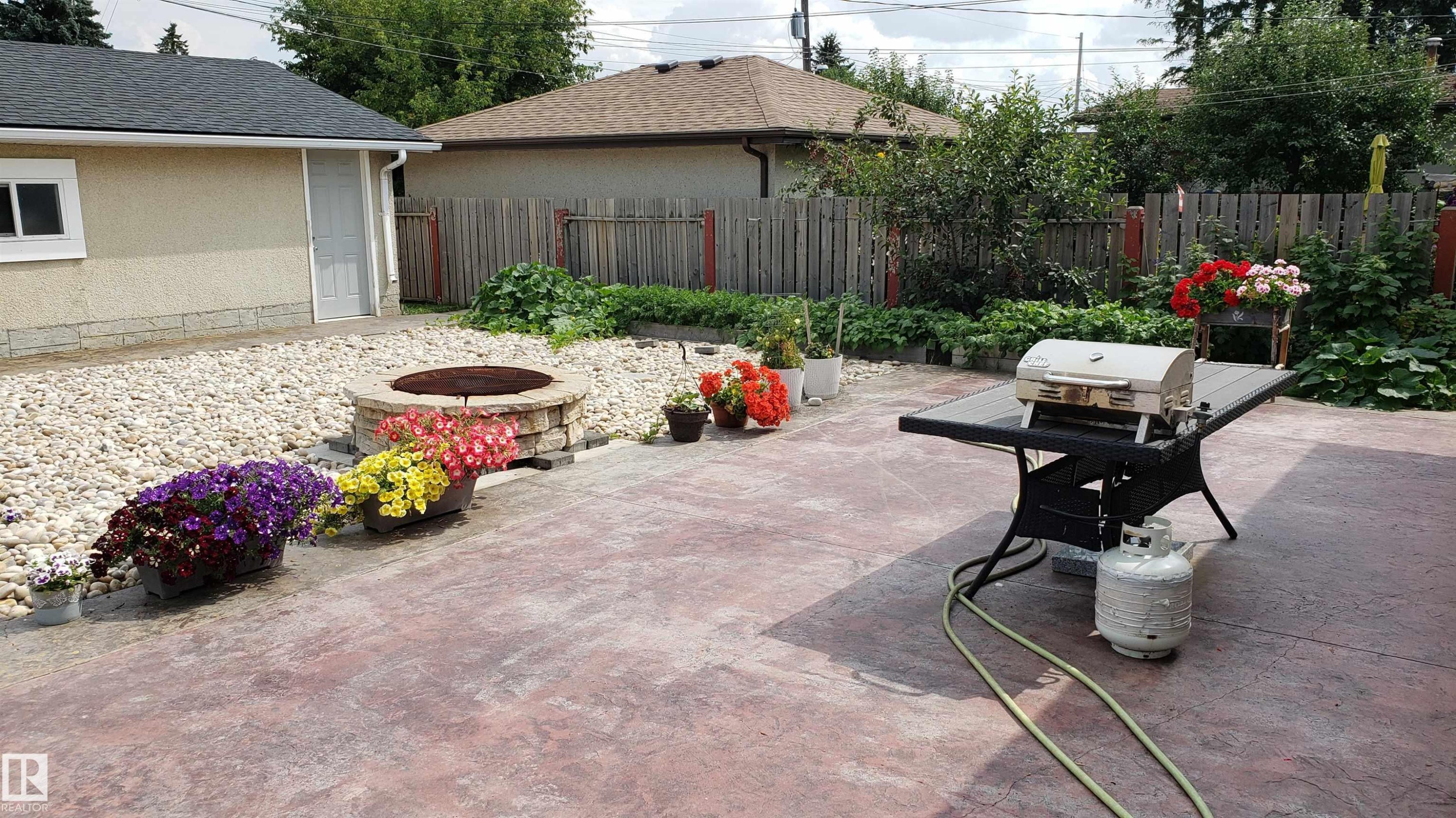 Spacious stamped concrete patio featuring a stone fire pit, gravel landscaping, and a detached garage with a side entry door - 13331 64 Street Nw, Edmonton, AB - Outdoor