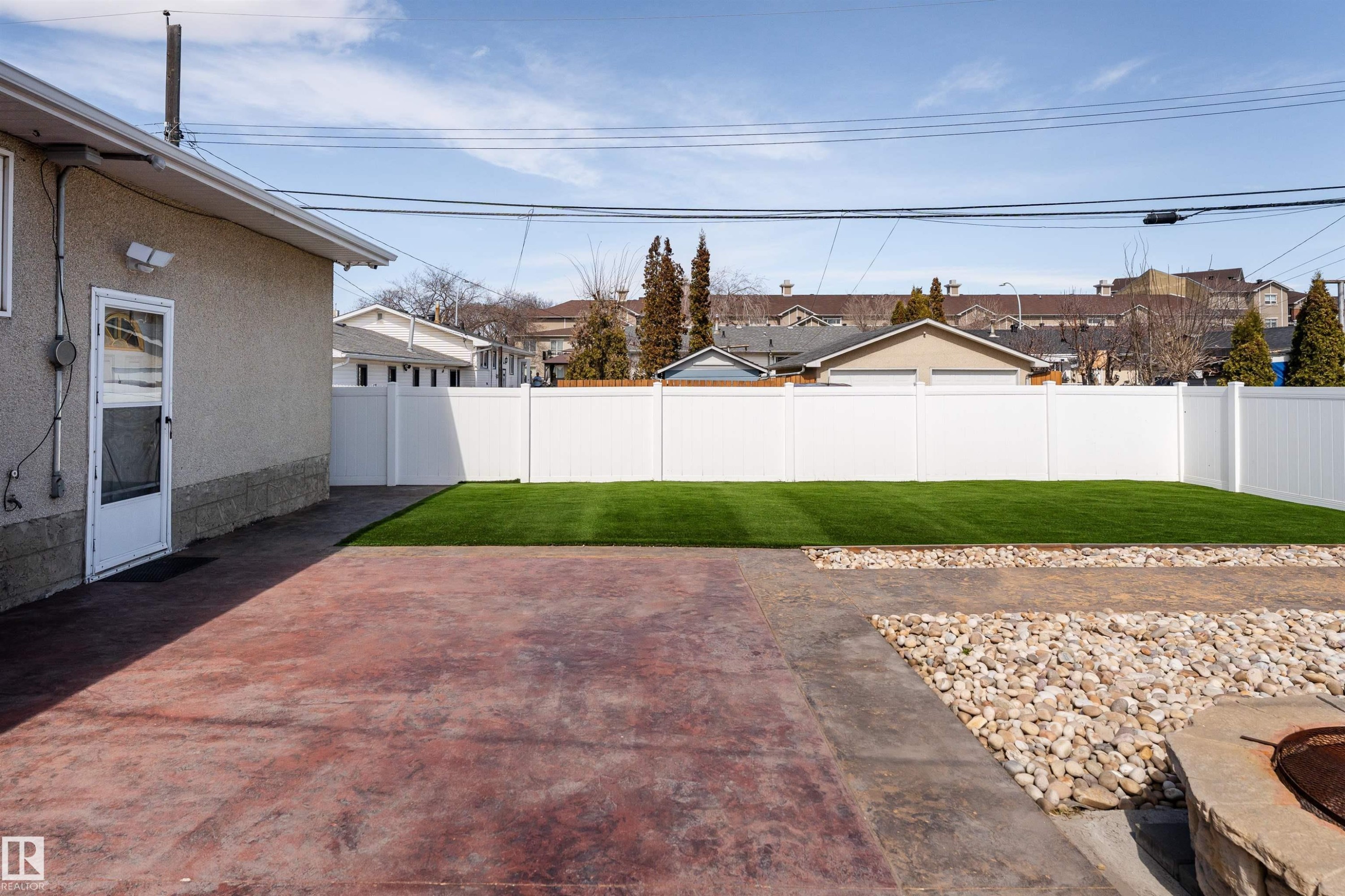 Private backyard featuring a vibrant artificial turf lawn, white vinyl fencing, a concrete patio, and a stone-edged fire pit - 13331 64 Street Nw, Edmonton, AB - Outdoor