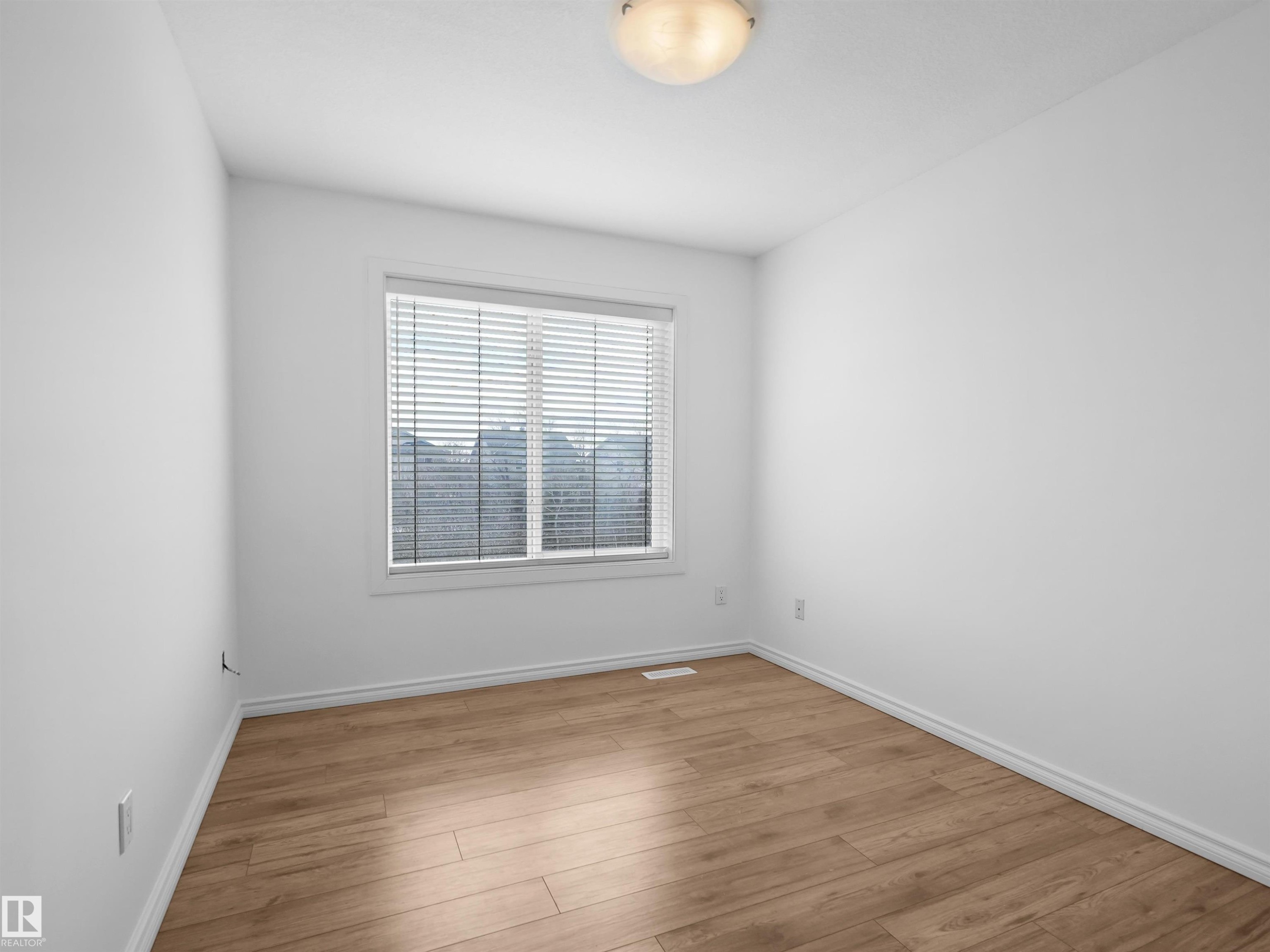 This room features light-toned hardwood flooring and crisp white walls, illuminated by a ceiling-mounted light fixture - #11 13215 153 Avenue, Edmonton, AB - Indoor Photo Showing Other Room