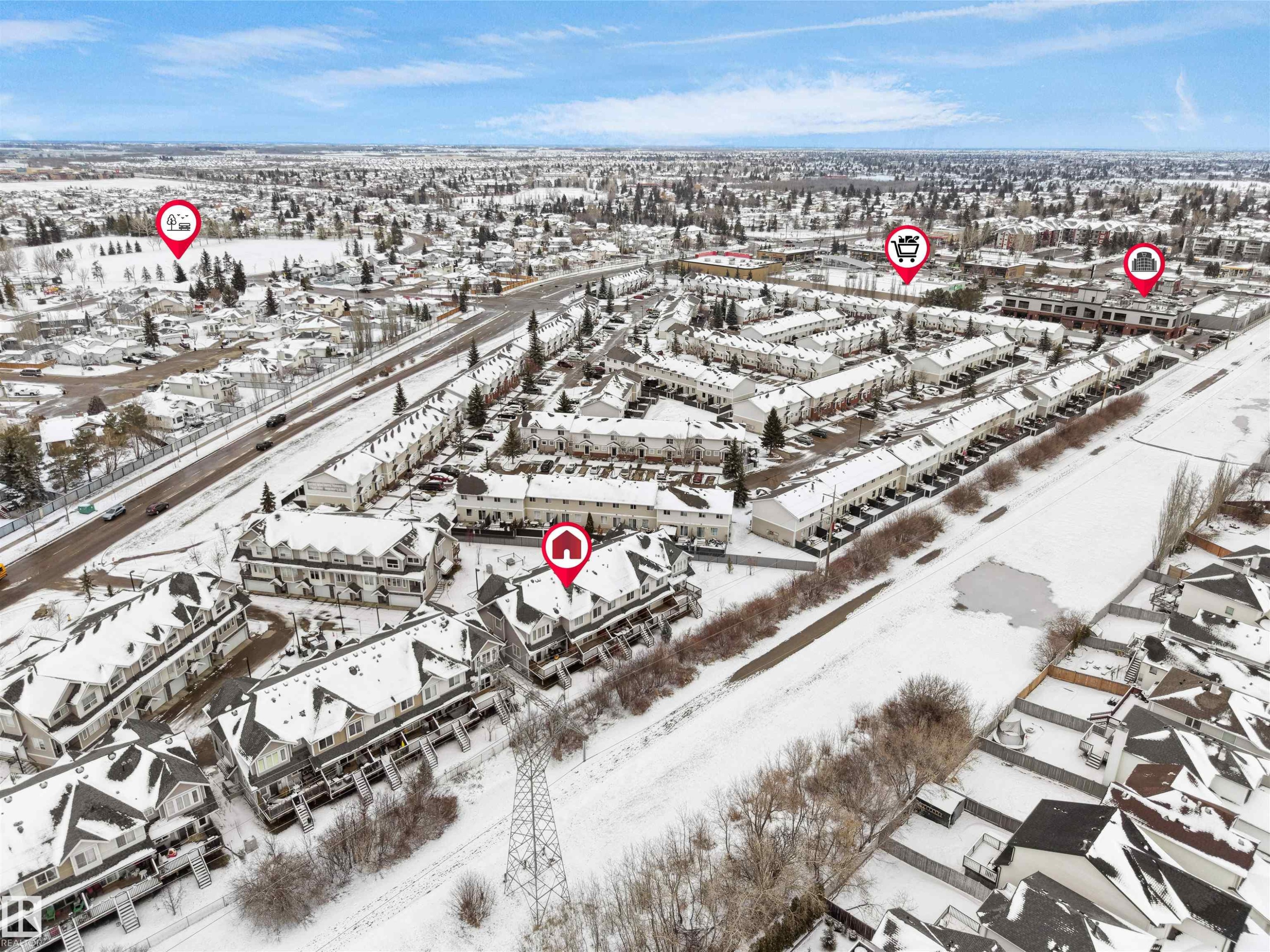 This aerial view highlights the property within a community featuring numerous residential structures, including townhomes and houses, all blanketed in snow - #11 13215 153 Avenue, Edmonton, AB - Outdoor With View