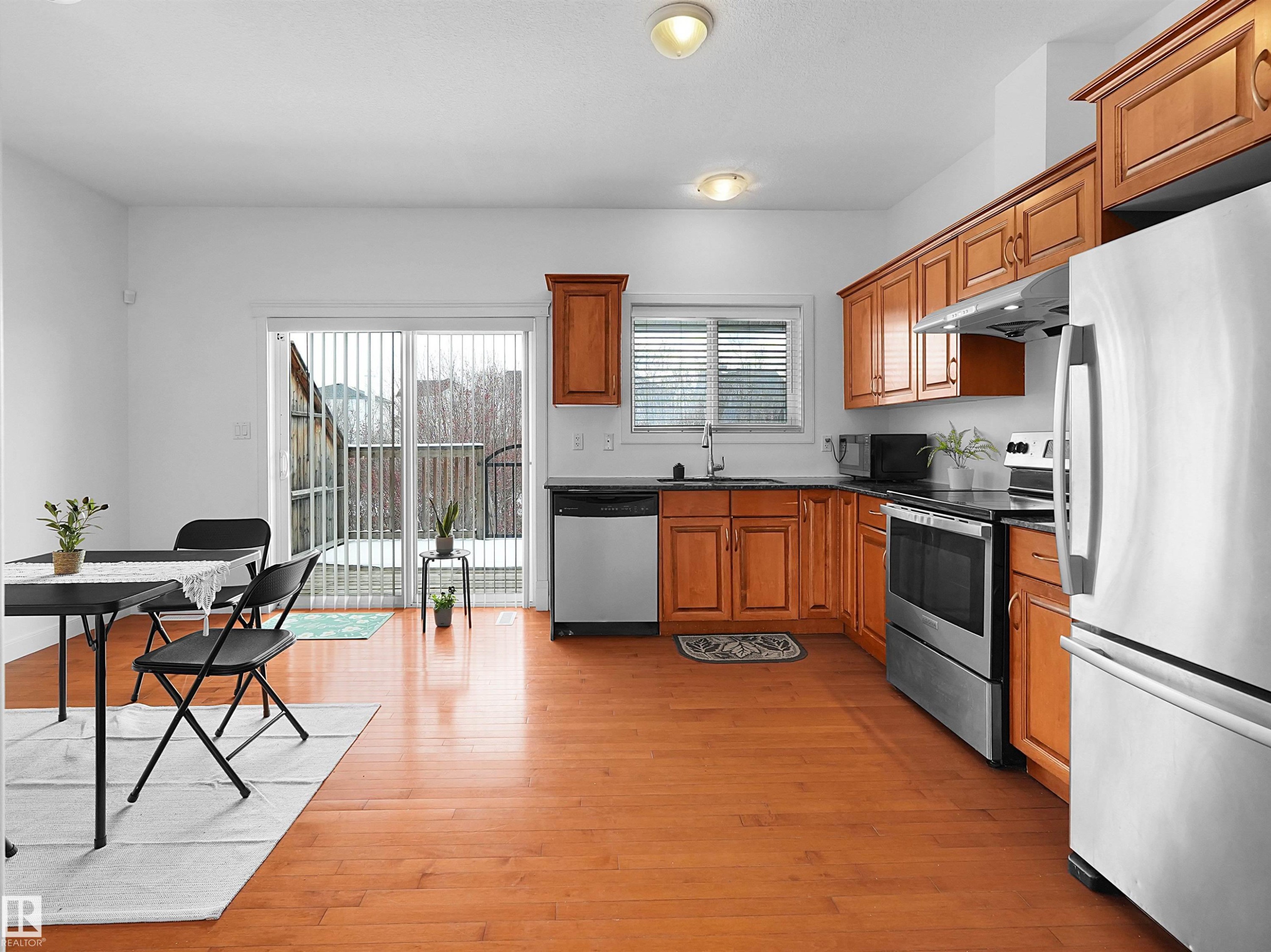 This kitchen features wood flooring, wooden cabinetry, and stainless steel appliances including a refrigerator, oven, and dishwasher - #11 13215 153 Avenue, Edmonton, AB - Indoor Photo Showing Kitchen With Double Sink