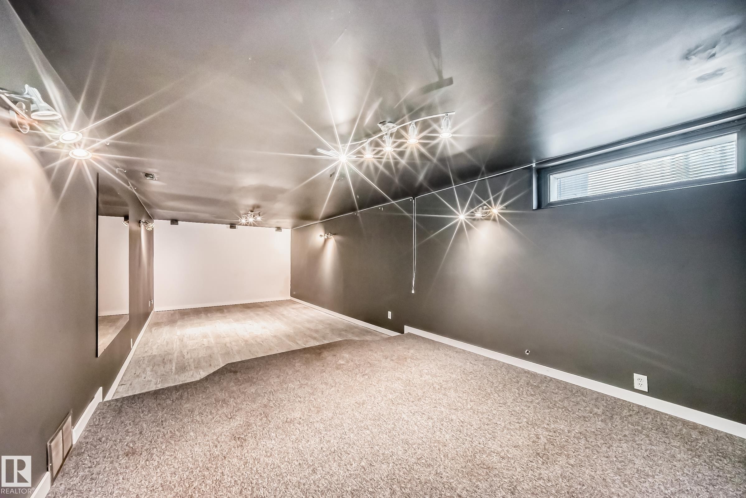 Spacious room with dark gray walls, white trim, and a combination of light-toned carpet and wood-finish flooring - 5204 112 Avenue Nw, Edmonton, AB - Indoor Photo Showing Other Room
