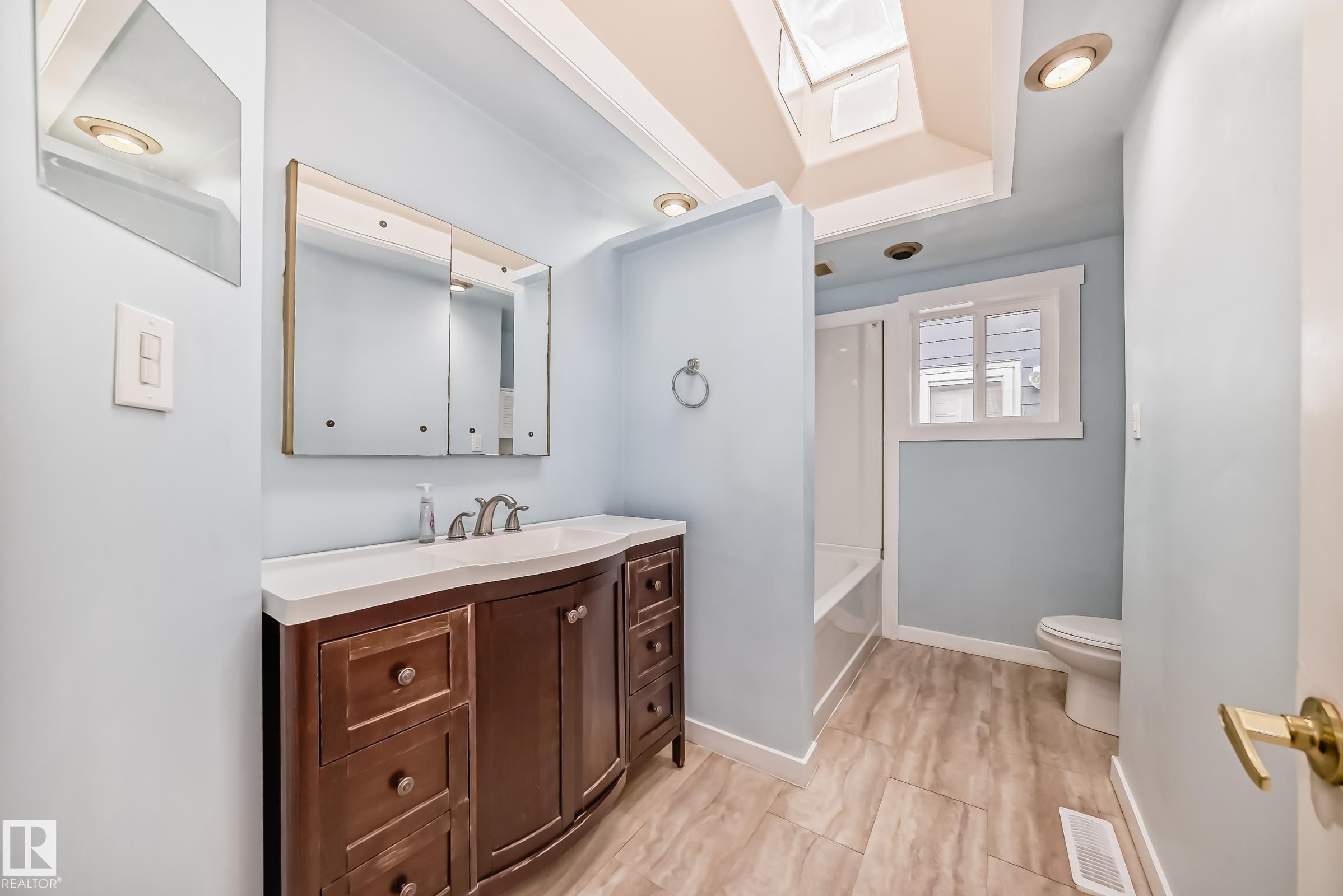 Bathroom featuring a wood-finish vanity with an integrated sink and countertop, a mirrored medicine cabinet, and a skylight - 5204 112 Avenue Nw, Edmonton, AB - Indoor Photo Showing Bathroom