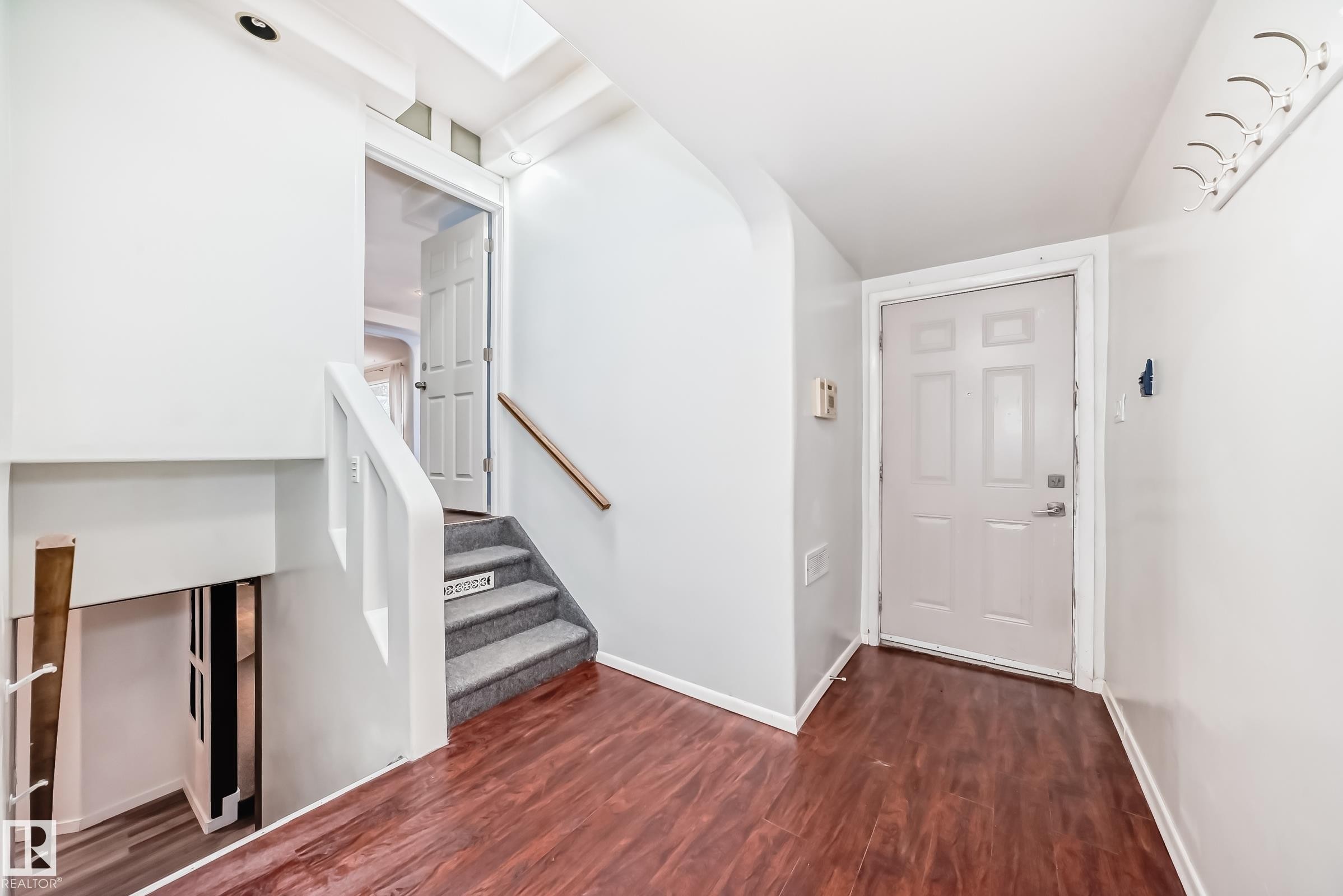 Foyer area featuring rich wood-finish flooring, a paneled entry door, and a staircase with gray carpeted treads - 5204 112 Avenue Nw, Edmonton, AB - Indoor Photo Showing Other Room