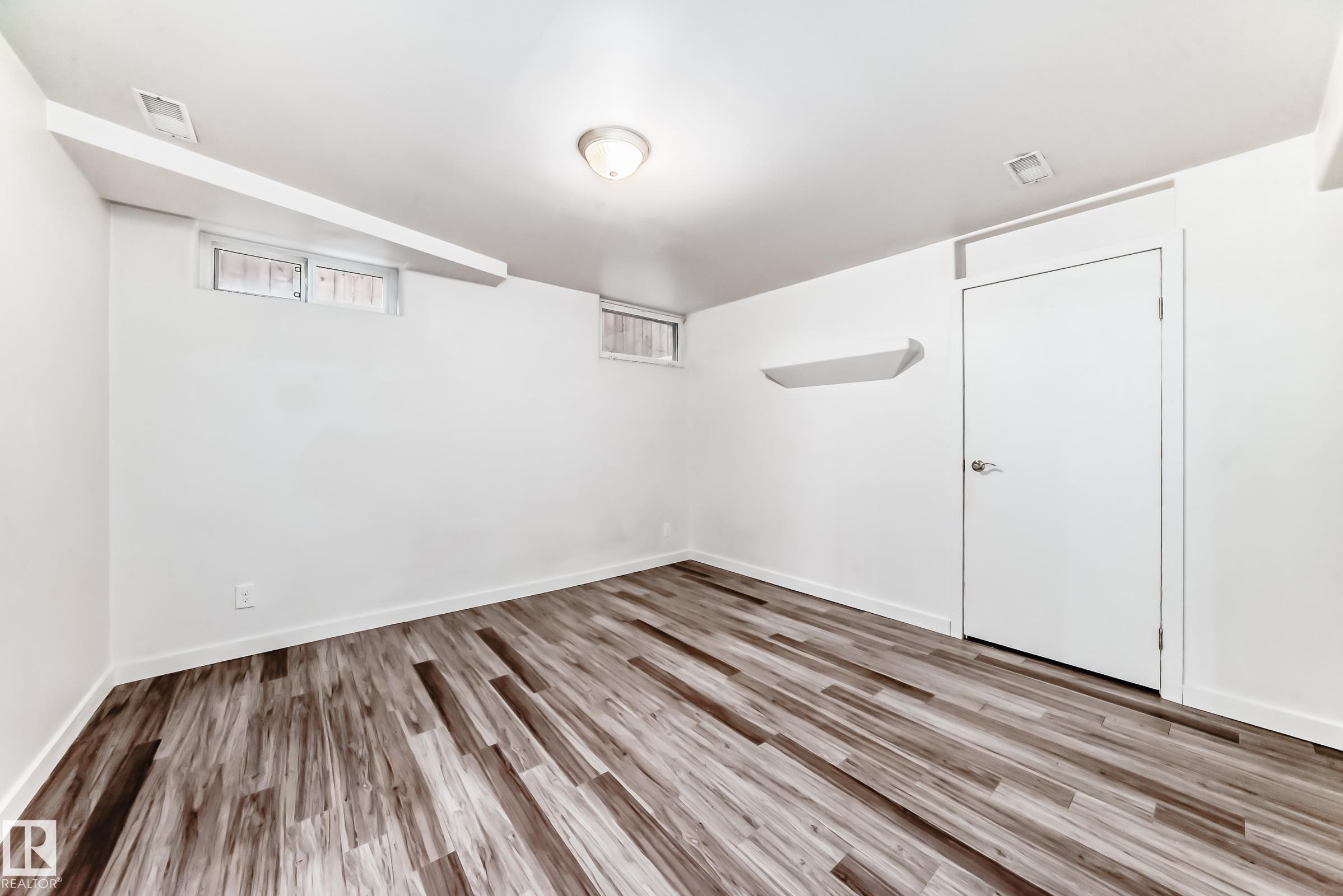 Spacious room featuring wood-finish flooring, white walls, and a ceiling-mounted light fixture - 5204 112 Avenue Nw, Edmonton, AB - Indoor Photo Showing Other Room