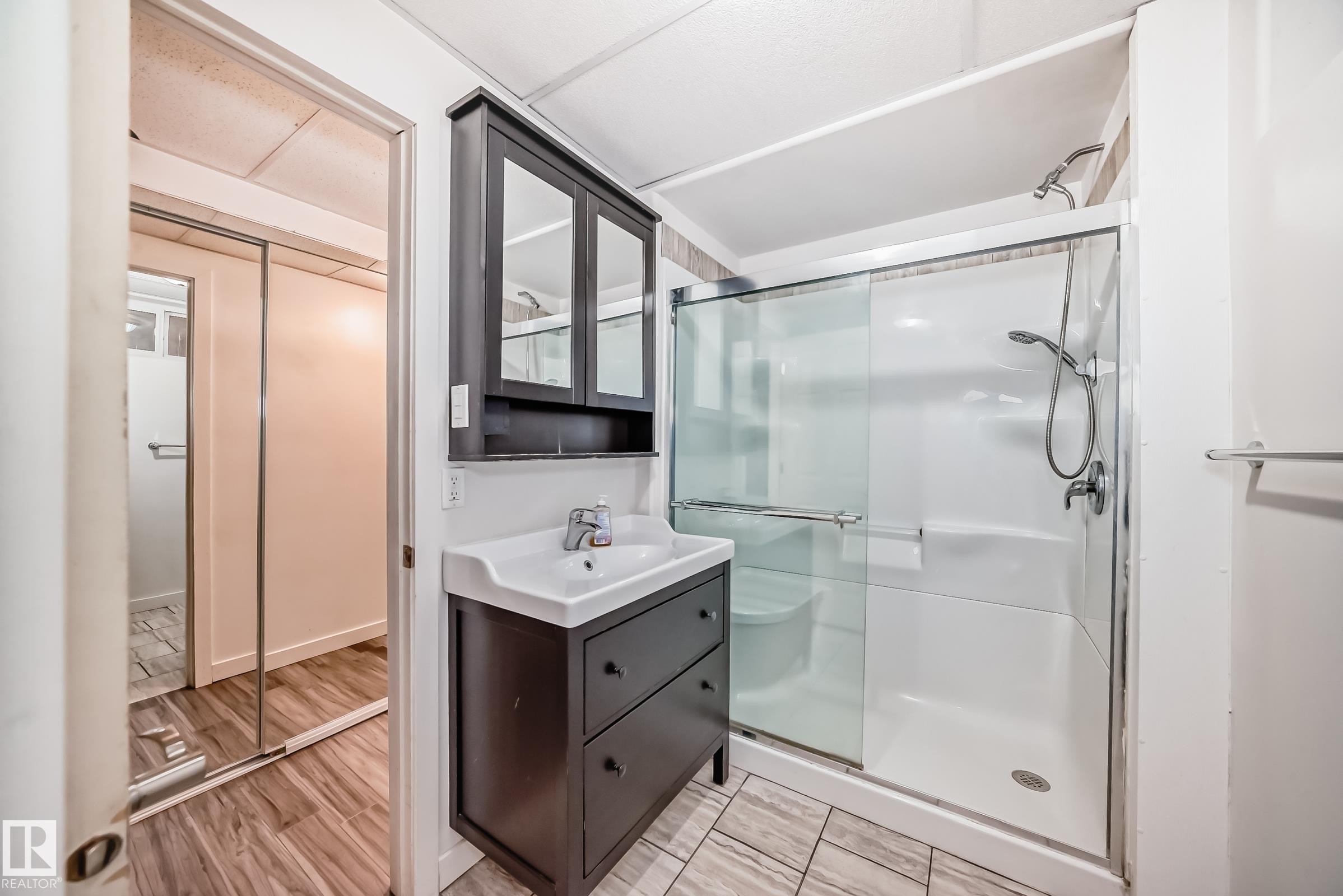 Bathroom featuring a dark wood-finish vanity with an integrated sink, a matching medicine cabinet with mirrored doors, and a glass-enclosed shower with a handheld showerhead - 5204 112 Avenue Nw, Edmonton, AB - Indoor Photo Showing Bathroom