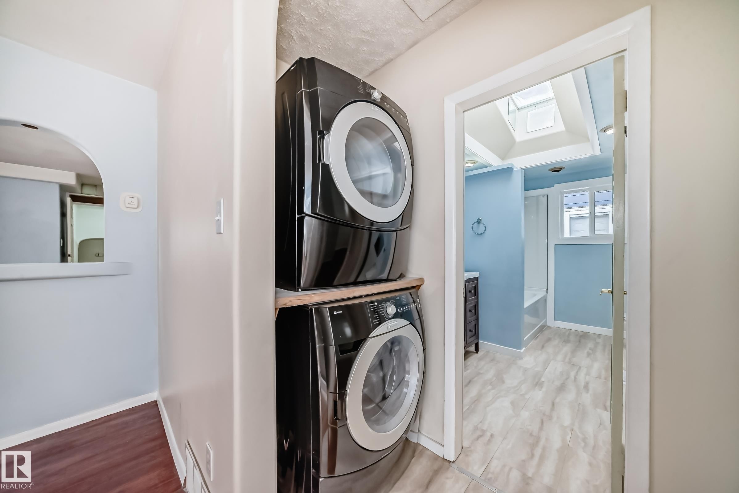 Dedicated laundry area featuring stacked appliances and wood-finish flooring - 5204 112 Avenue Nw, Edmonton, AB - Indoor Photo Showing Laundry Room
