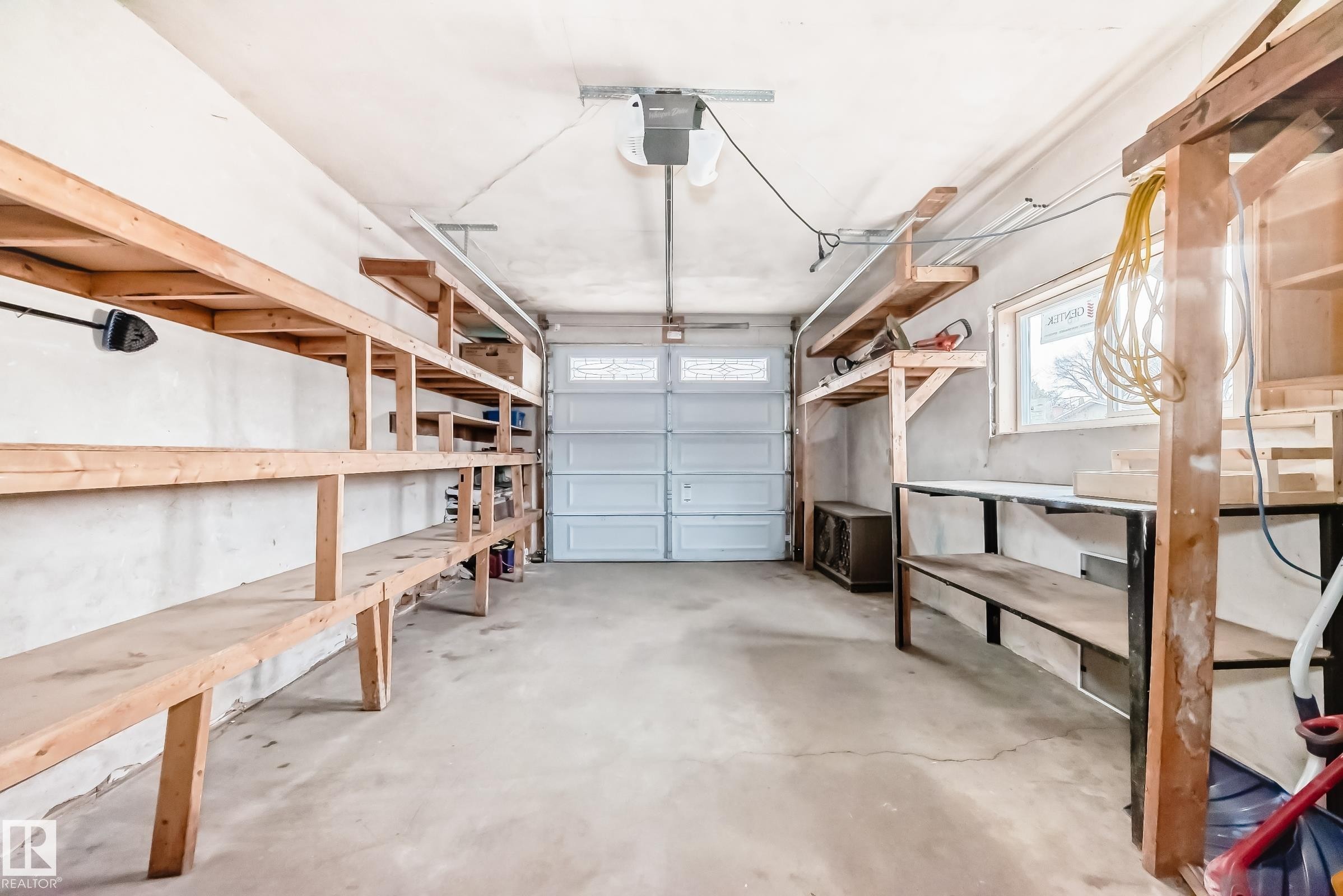 Attached garage featuring a concrete floor, built-in shelving, a window providing natural light, and a white panel garage door with upper window inserts - 5204 112 Avenue Nw, Edmonton, AB - Indoor Photo Showing Garage