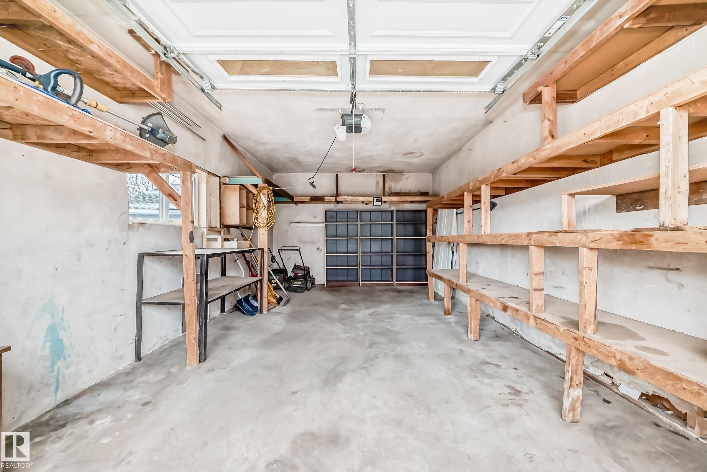 Spacious garage featuring a concrete floor, overhead garage door, built-in wooden shelving, a window, and a dedicated storage area - 5204 112 Avenue Nw, Edmonton, AB - Indoor Photo Showing Garage