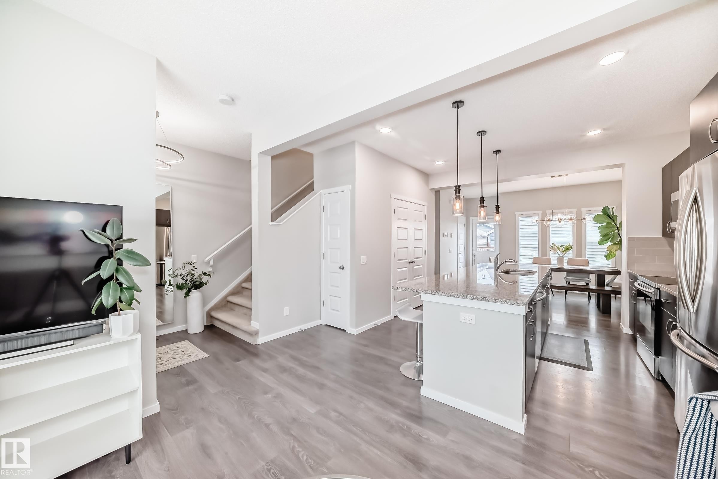 Open concept living area featuring wood-finish flooring, a kitchen island with pendant lighting, stainless steel appliances, and a dining area with multiple windows - 3278 Cherry Crescent, Edmonton, AB - Indoor Photo Showing Kitchen With Upgraded Kitchen