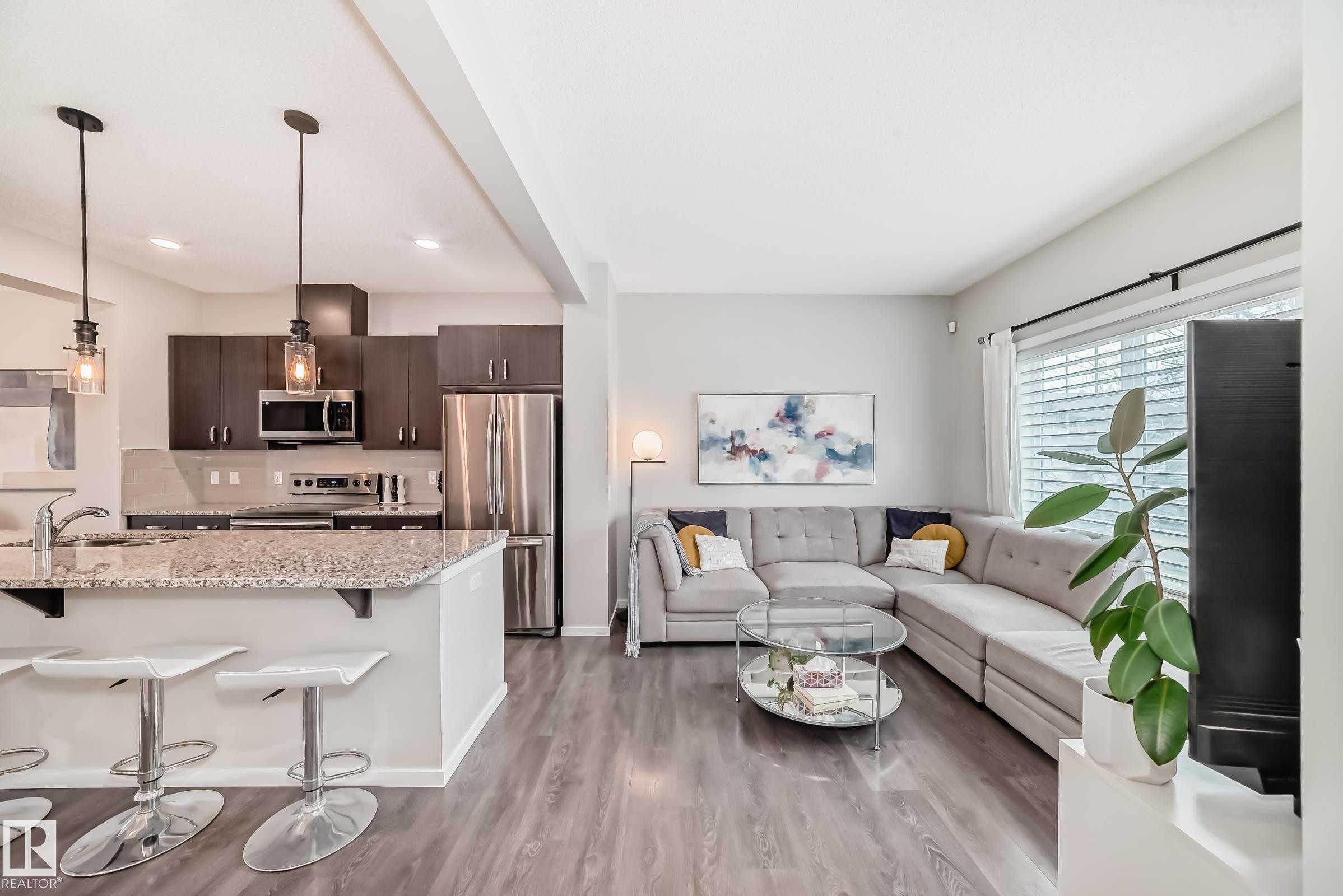 Open-concept living space featuring wood-finish flooring, a kitchen island with stone countertop, stainless steel appliances, dark wood cabinetry, and recessed lighting - 3278 Cherry Crescent, Edmonton, AB - Indoor Photo Showing Kitchen With Upgraded Kitchen
