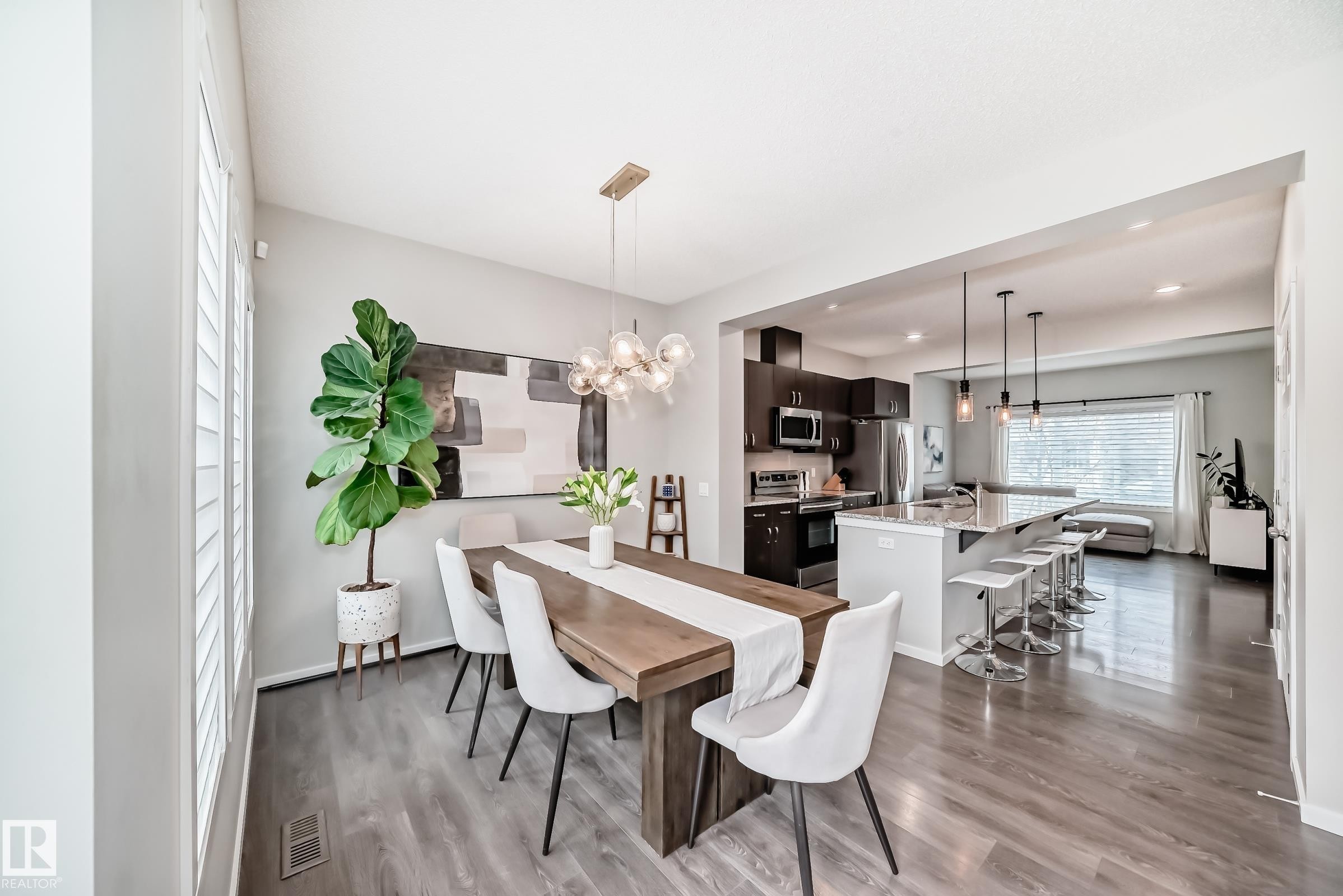 Open-concept dining area featuring wood-finish flooring, a contemporary chandelier, and plantation shutters - 3278 Cherry Crescent, Edmonton, AB - Indoor Photo Showing Dining Room
