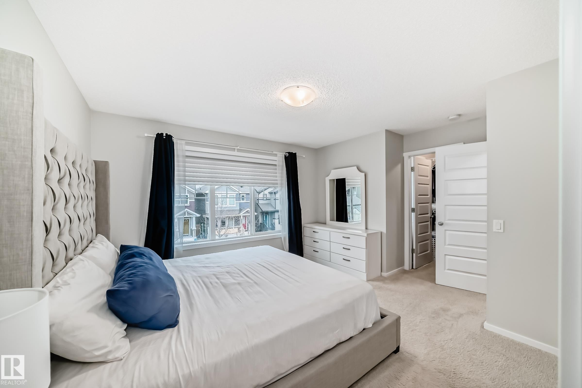 Carpeted bedroom featuring a large window with blinds and dark curtains, a ceiling-mounted light fixture, light gray wall paint, and a white paneled door - 3278 Cherry Crescent, Edmonton, AB - Indoor Photo Showing Bedroom