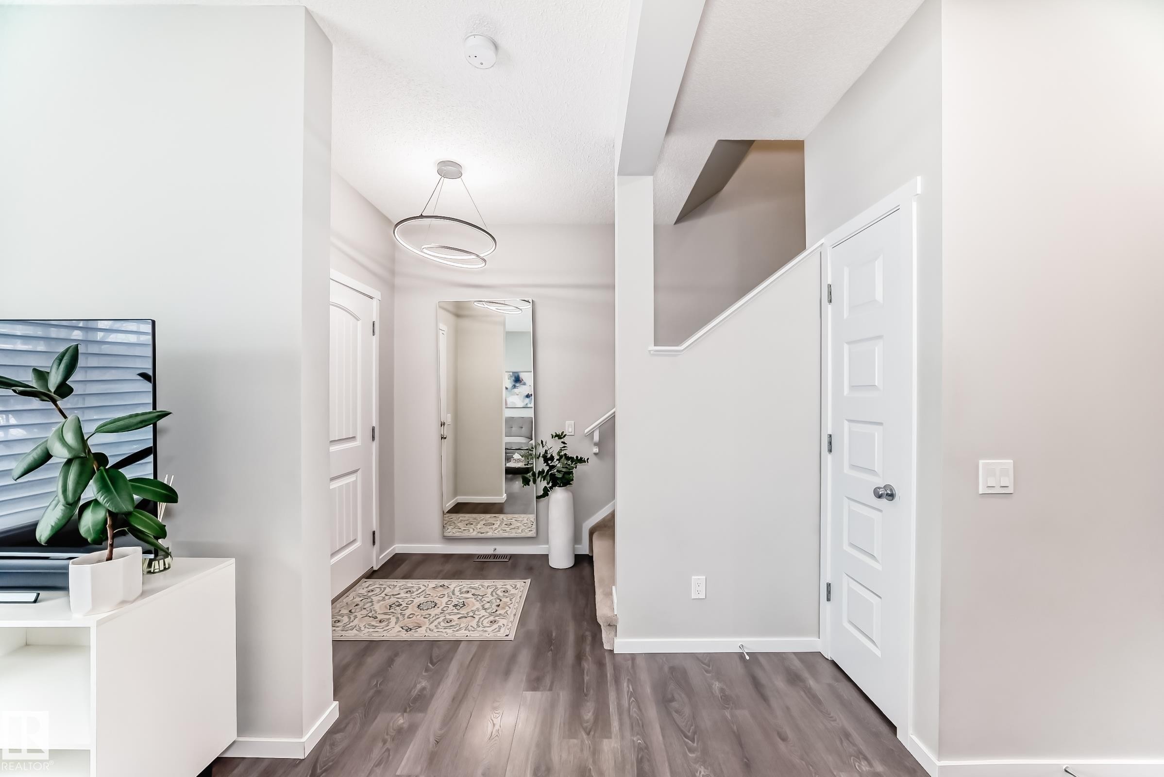 Entryway featuring wood-finish flooring, a modern circular pendant light fixture, and a staircase with carpeted treads - 3278 Cherry Crescent, Edmonton, AB - Indoor Photo Showing Other Room