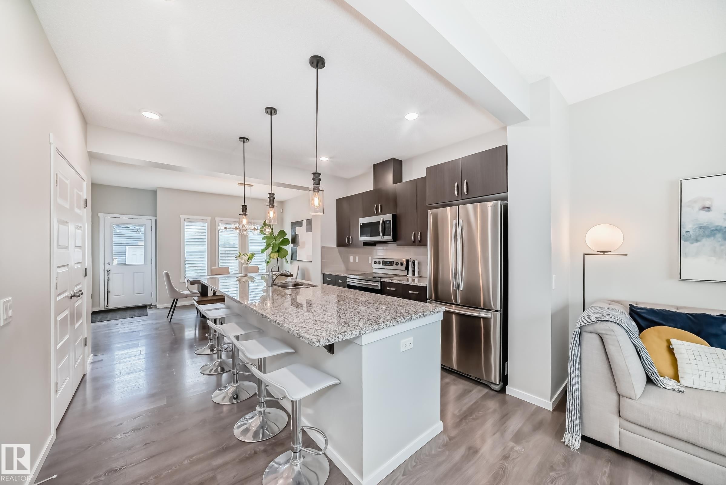 Open-concept kitchen featuring an oversized island with a granite countertop, dark wood-finish cabinetry, and stainless steel appliances - 3278 Cherry Crescent, Edmonton, AB - Indoor Photo Showing Kitchen With Upgraded Kitchen