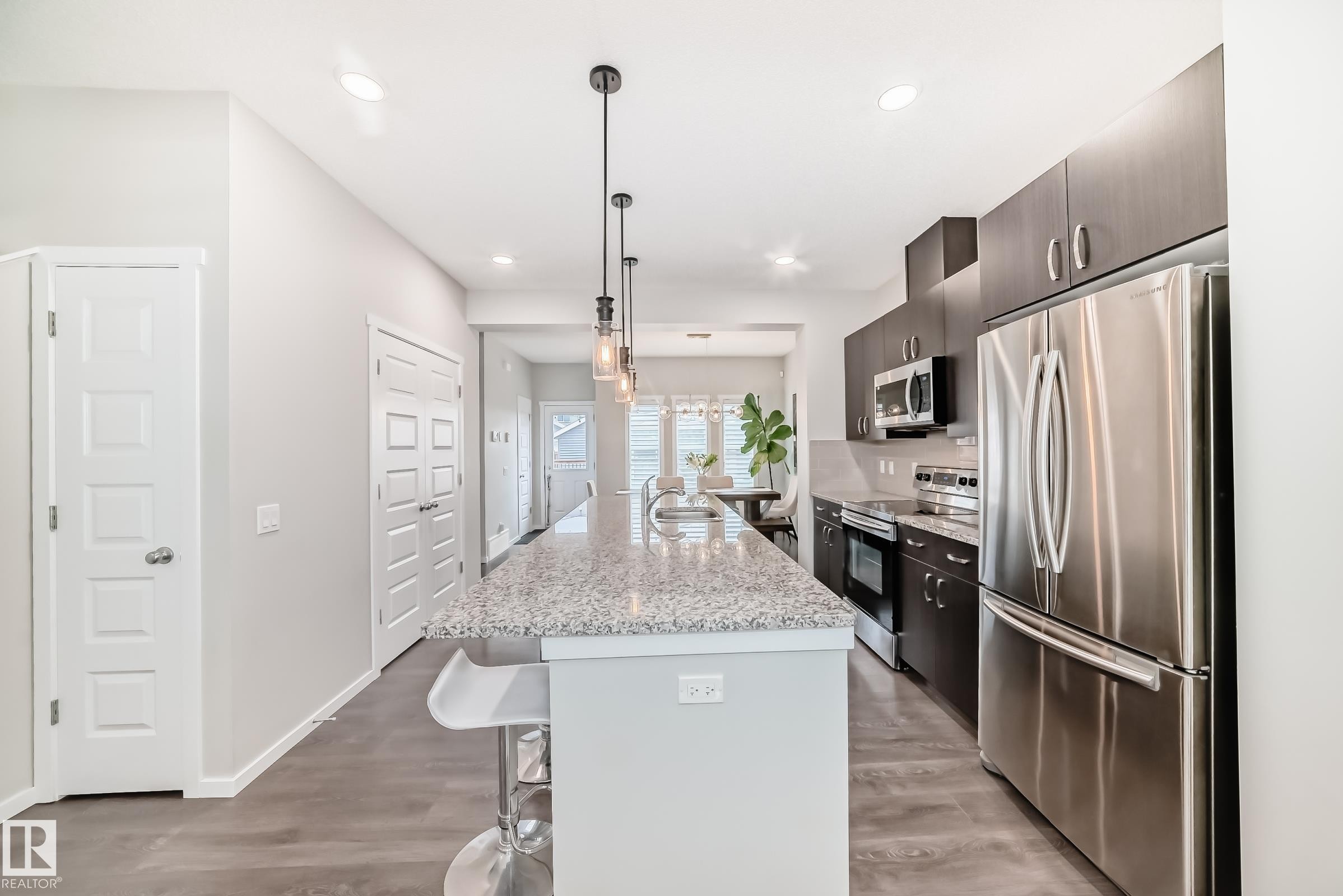 Contemporary kitchen featuring dark wood-finish cabinetry, stainless steel appliances, and a spacious island with a light speckled countertop - 3278 Cherry Crescent, Edmonton, AB - Indoor Photo Showing Kitchen With Upgraded Kitchen