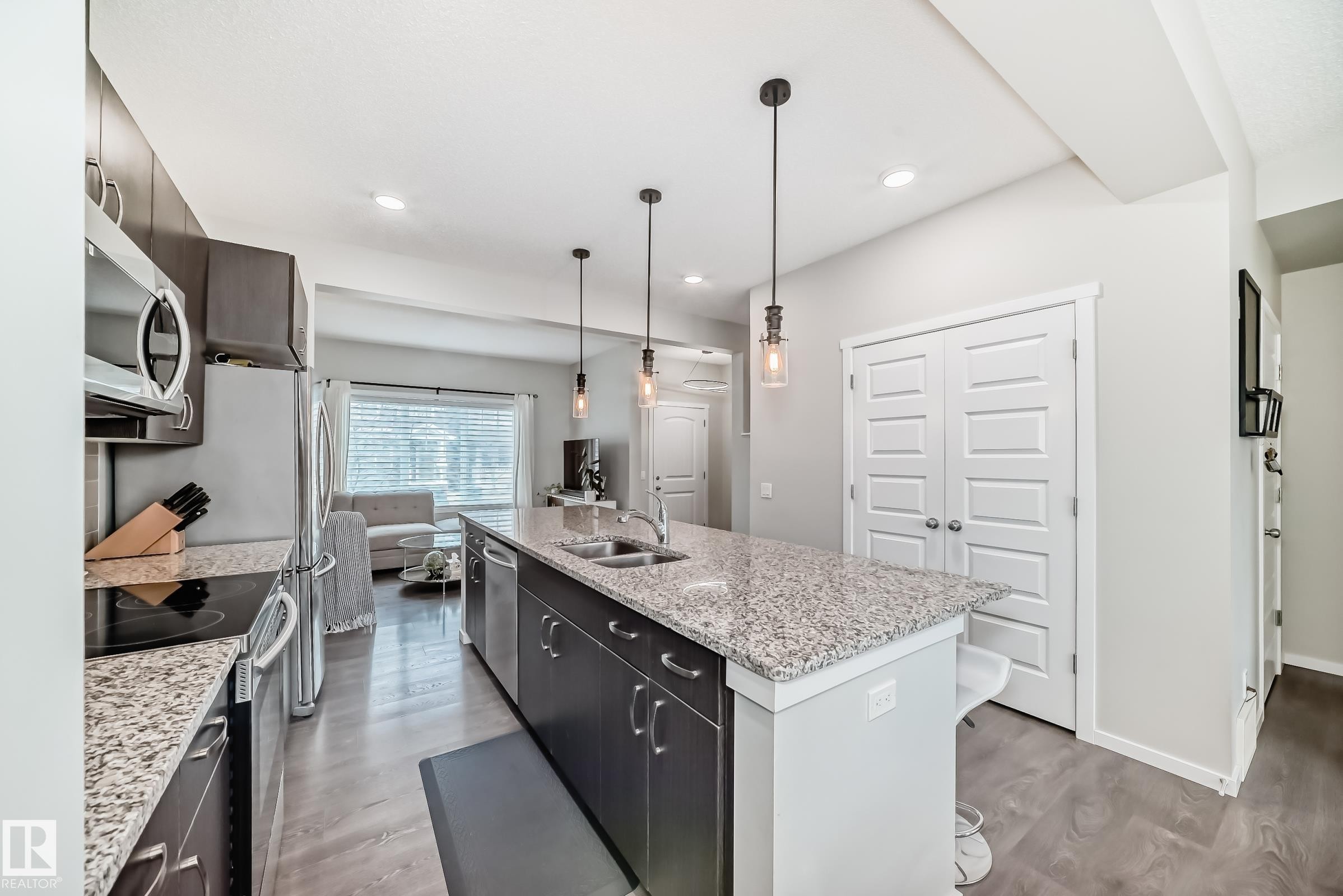 Modern kitchen featuring a large island with granite-finish countertop, stainless steel appliances, dark wood-finish cabinetry, and recessed lighting - 3278 Cherry Crescent, Edmonton, AB - Indoor Photo Showing Kitchen With Double Sink With Upgraded Kitchen