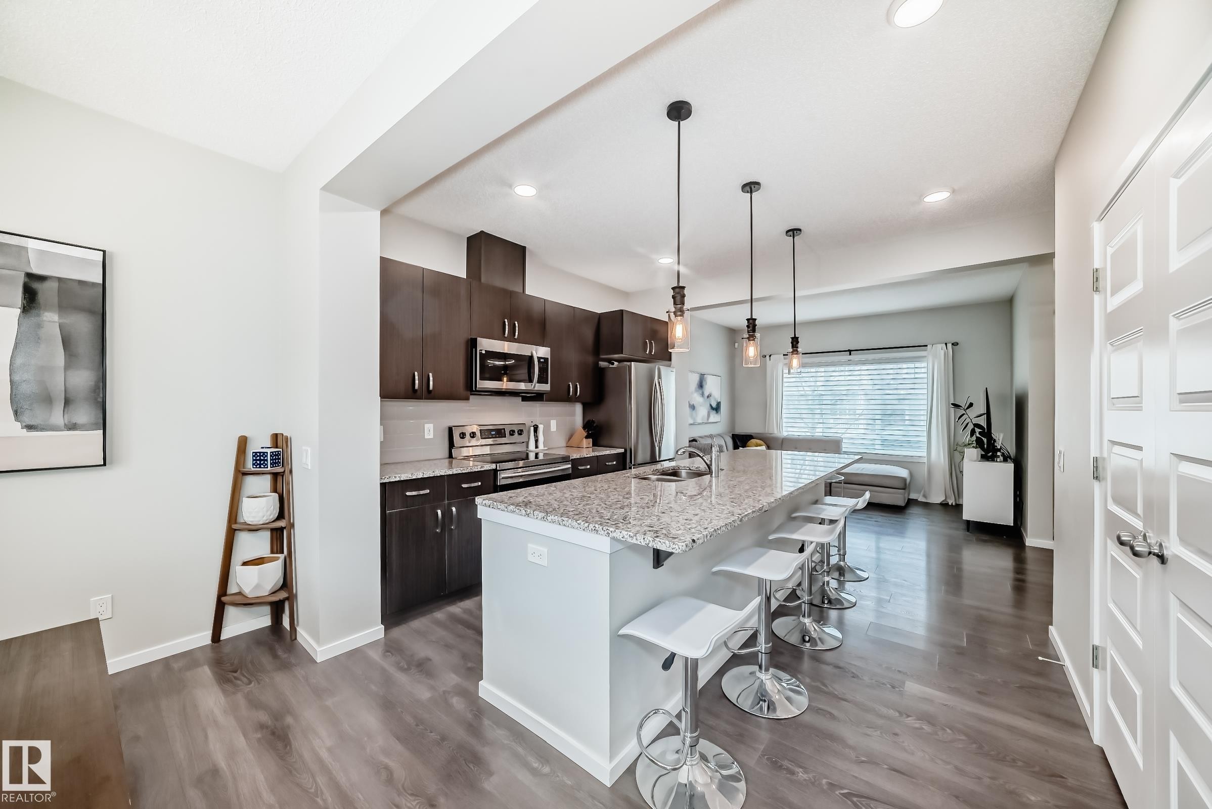 Open-concept kitchen featuring dark wood cabinetry, stainless steel appliances, and a light granite island with pendant lighting - 3278 Cherry Crescent, Edmonton, AB - Indoor Photo Showing Kitchen With Upgraded Kitchen