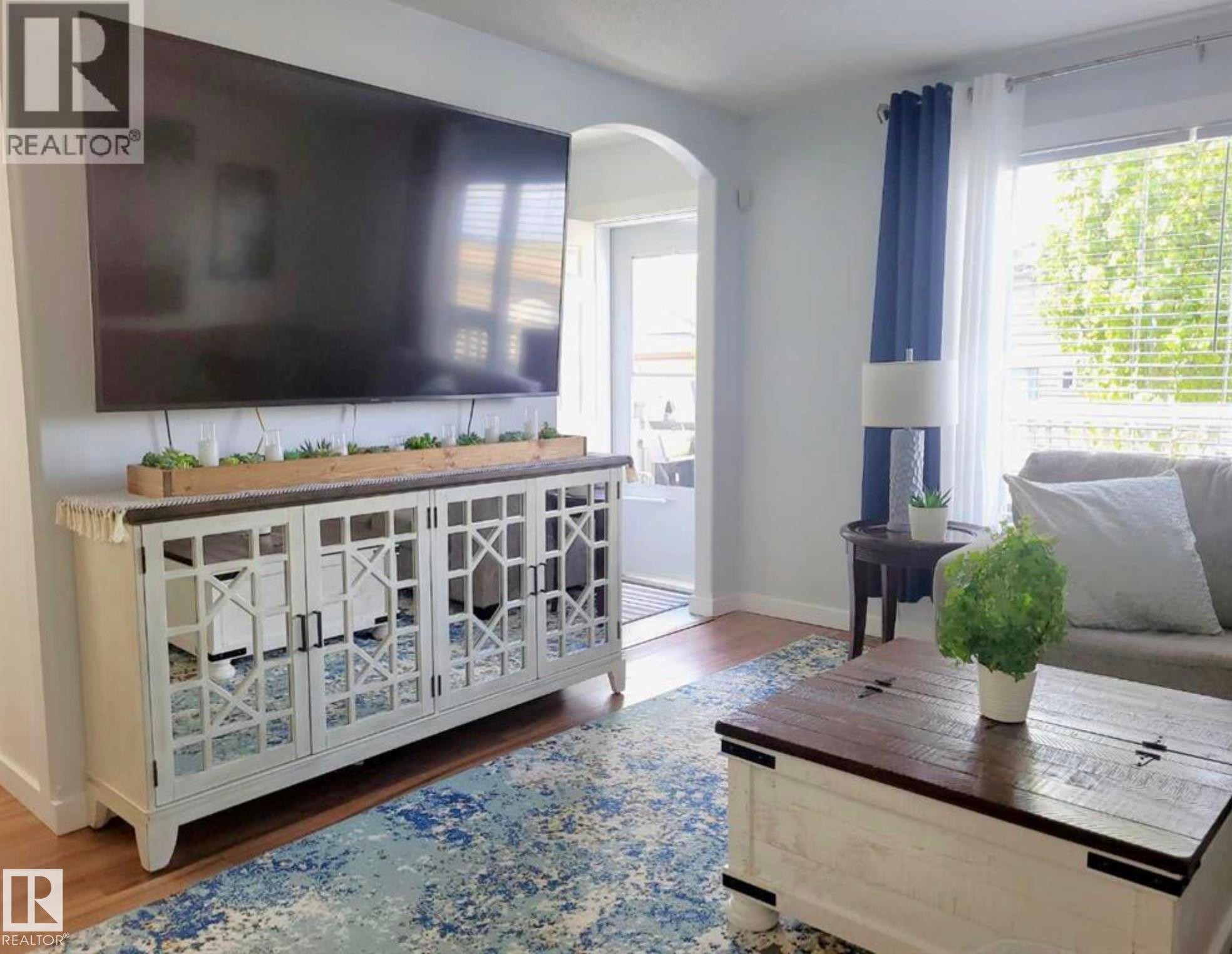 Spacious living area featuring wood-finish flooring, an arched doorway, and ample natural light from a large window with blinds - 144 Kirpatrick Way, Leduc, AB - Indoor Photo Showing Living Room