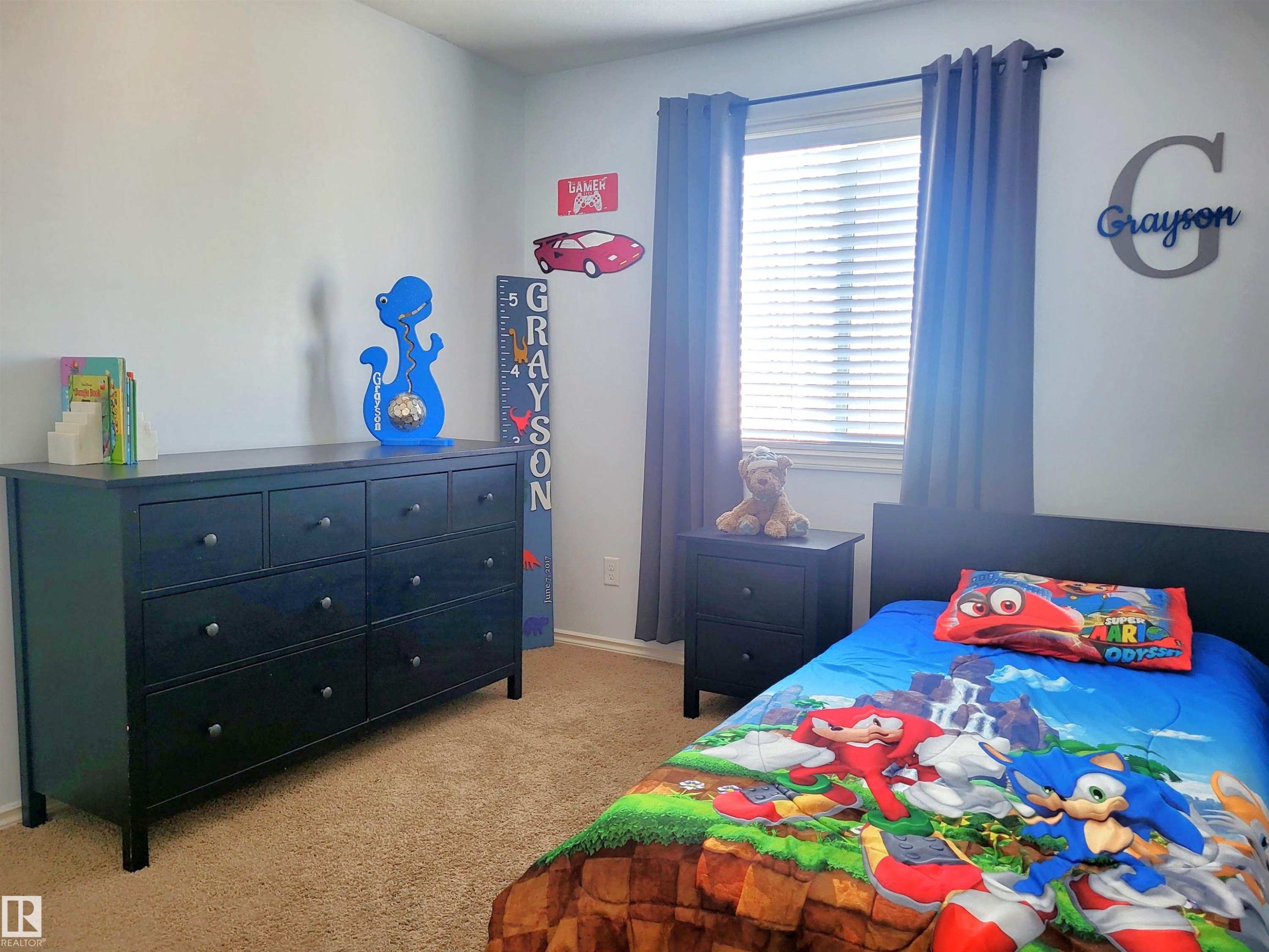 Carpeted room featuring a window with blinds and gray curtains, a dark wood-finish dresser with nine drawers, and a coordinating nightstand with two drawers - 144 Kirpatrick Way, Leduc, AB - Indoor Photo Showing Bedroom