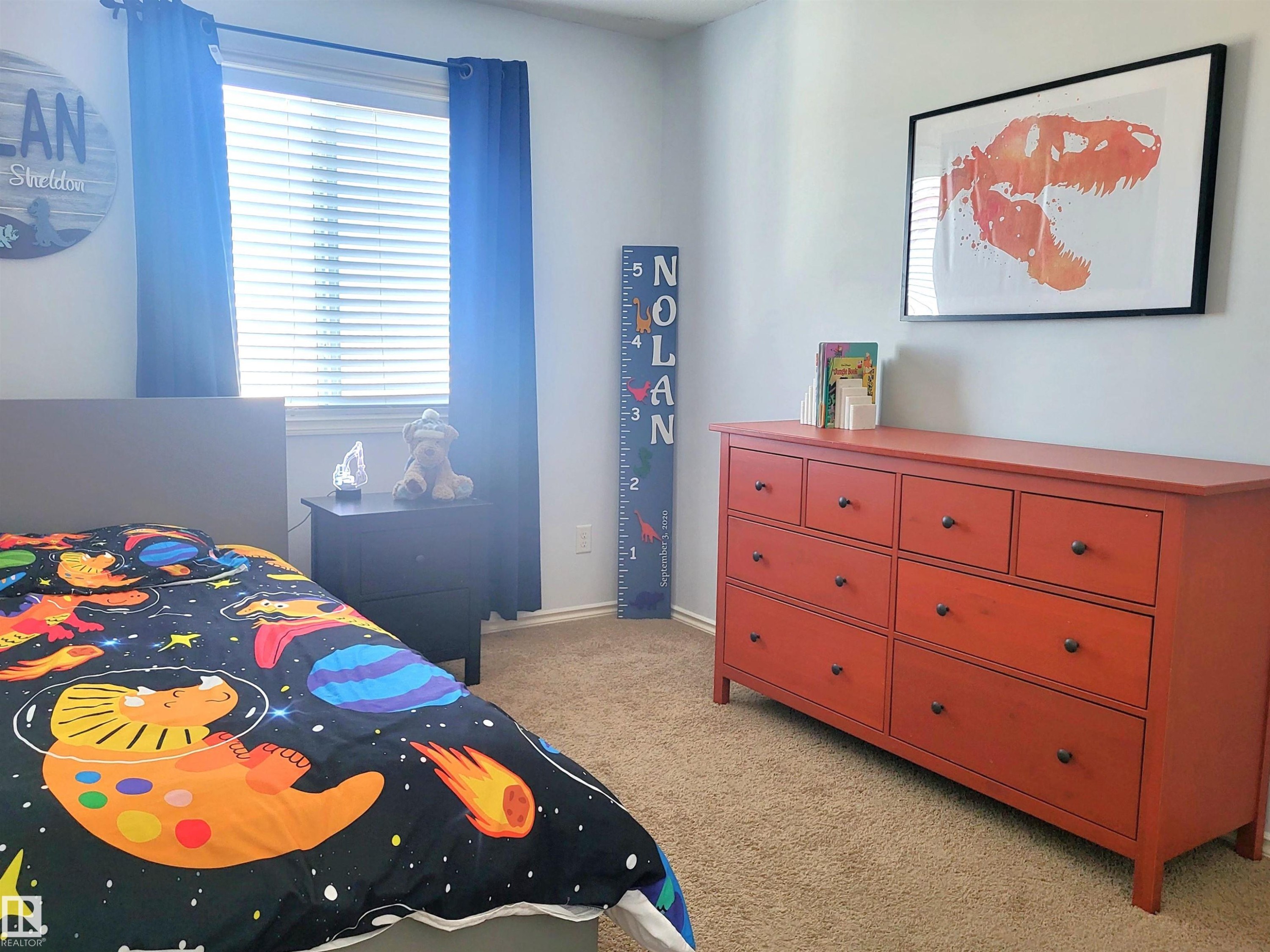Carpeted room with a double-paned window featuring horizontal blinds and blue curtain panels - 144 Kirpatrick Way, Leduc, AB - Indoor Photo Showing Bedroom