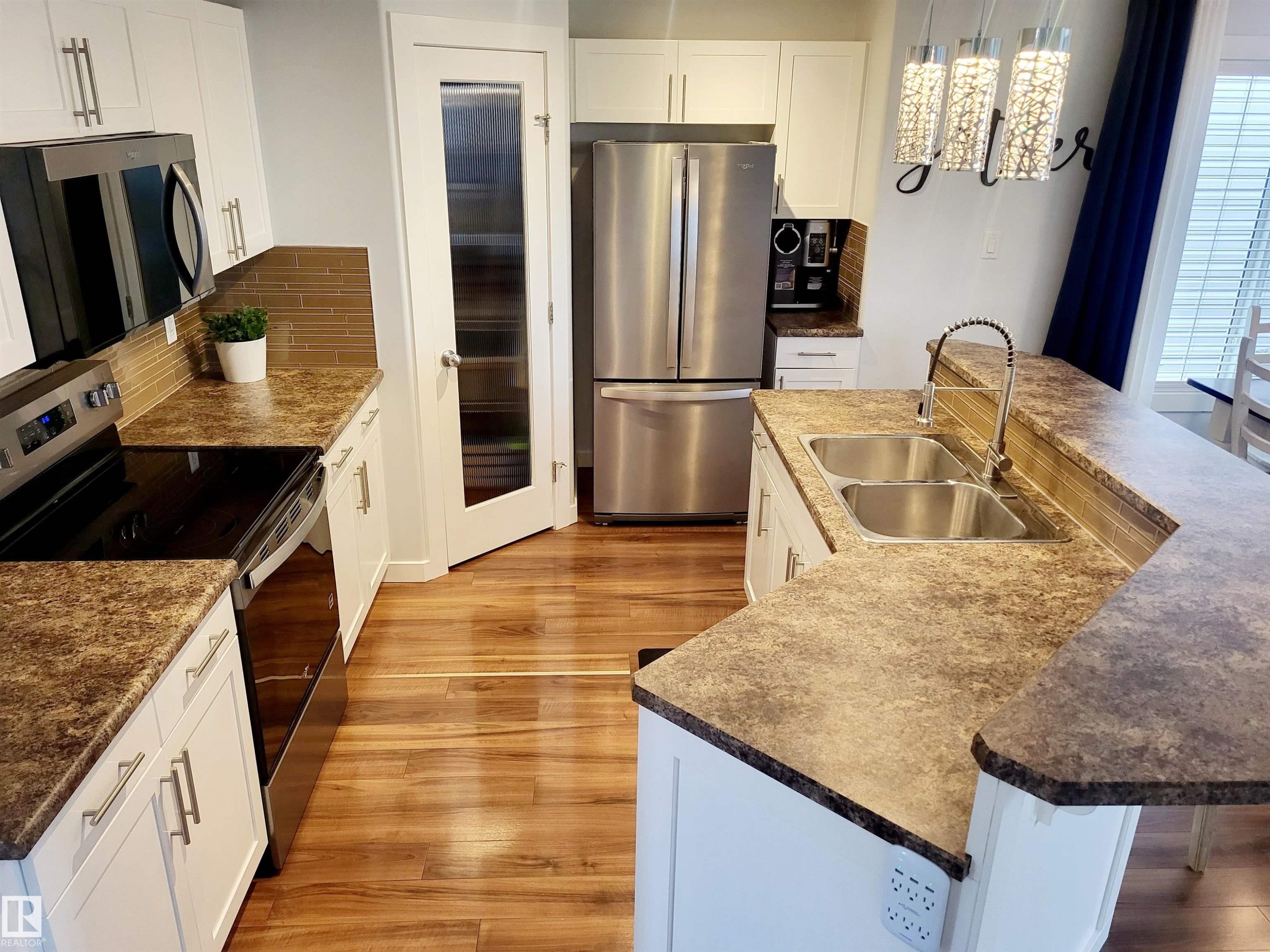 Modern kitchen featuring wood-finish flooring, white cabinetry with brushed nickel hardware, a stainless steel double-basin sink, and a glass-paneled pantry door - 144 Kirpatrick Way, Leduc, AB - Indoor Photo Showing Kitchen With Stainless Steel Kitchen With Double Sink