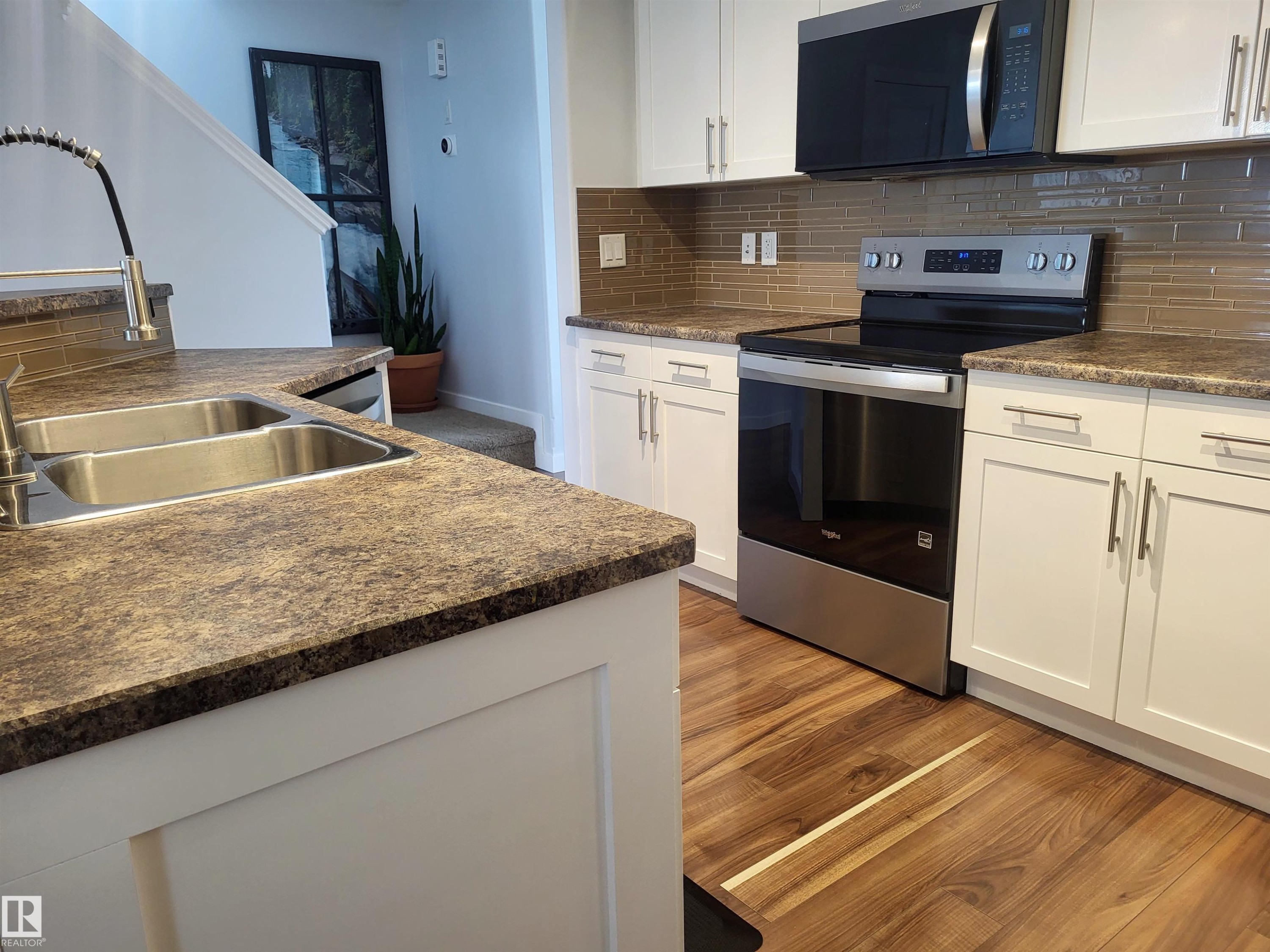 Modern kitchen featuring white cabinetry with brushed nickel hardware, a stainless steel double basin sink, and a high-arc faucet - 144 Kirpatrick Way, Leduc, AB - Indoor Photo Showing Kitchen With Double Sink