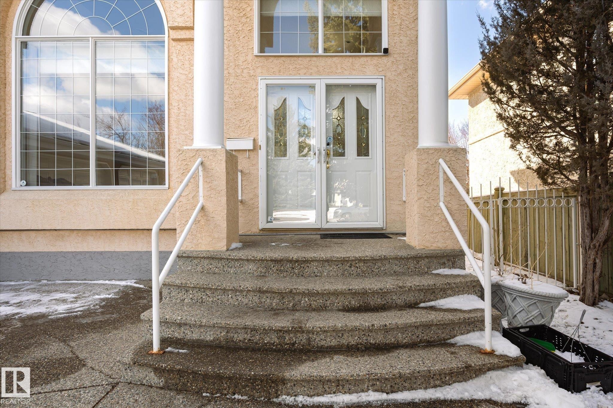 The property features a double front door with decorative glass inserts, flanked by two substantial columns and a large arched window with grid detailing - 128 Weaver Drive, Edmonton, AB - Outdoor