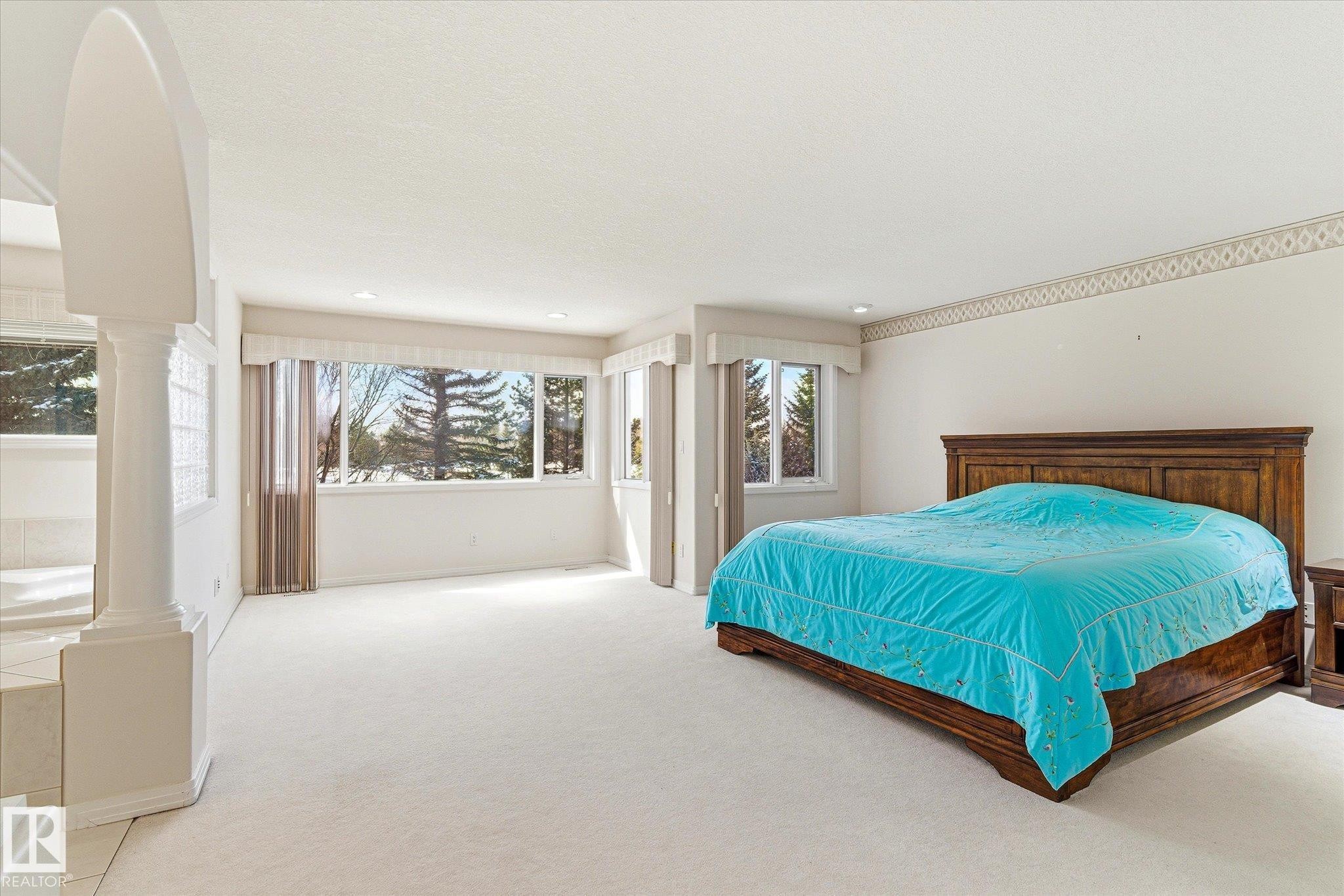 This spacious area features light-colored carpeting, large windows offering views of exterior trees, and recessed lighting - 128 Weaver Drive, Edmonton, AB - Indoor Photo Showing Bedroom