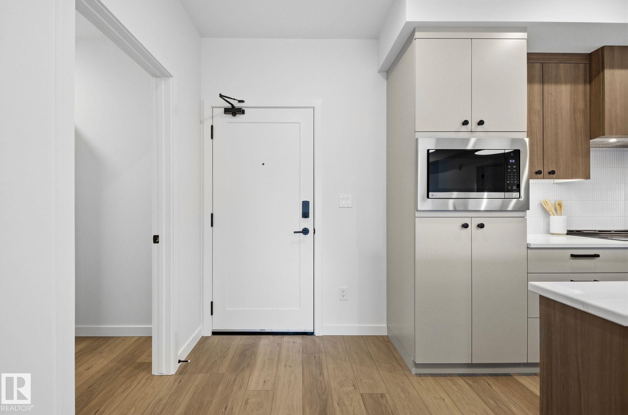 Wood-finish flooring throughout, bright white walls, modern kitchen cabinetry in two-tone finishes, stainless steel built-in microwave, and white subway tile backsplash - 202 7459 May Common, Edmonton, AB - Indoor