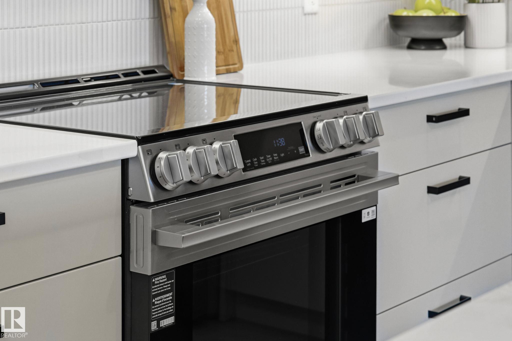 Stainless steel range with a glass cooktop, surrounded by light-toned cabinetry featuring matte black hardware, white countertops, and a fluted tile backsplash - 202 7459 May Common, Edmonton, AB - Indoor Photo Showing Kitchen