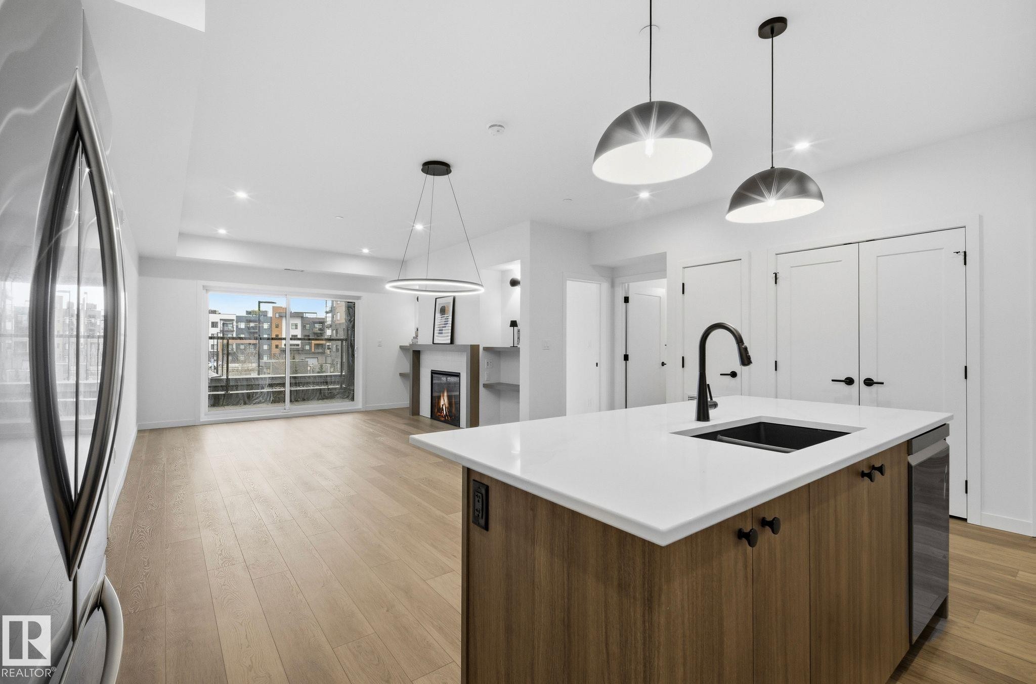Contemporary kitchen island with a white countertop, undermount sink, and matte black faucet - 202 7459 May Common, Edmonton, AB - Indoor Photo Showing Kitchen With Upgraded Kitchen